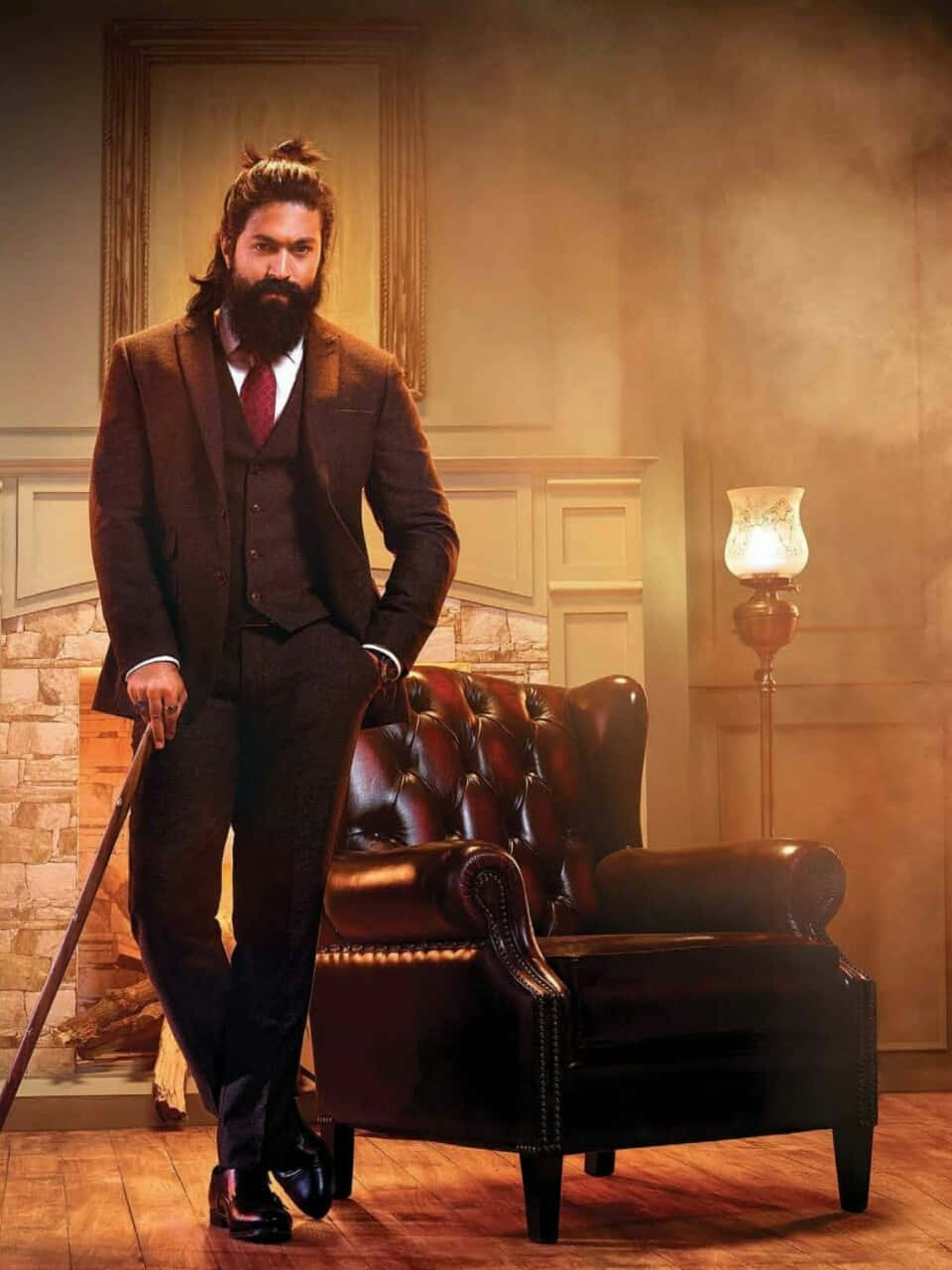 Kgf 2 桌布 壁紙 — 一位留鬍鬚的男人穿著棕色西裝，自信地靠在一張皮革扶手椅上，身處溫暖燈光的復古書房。