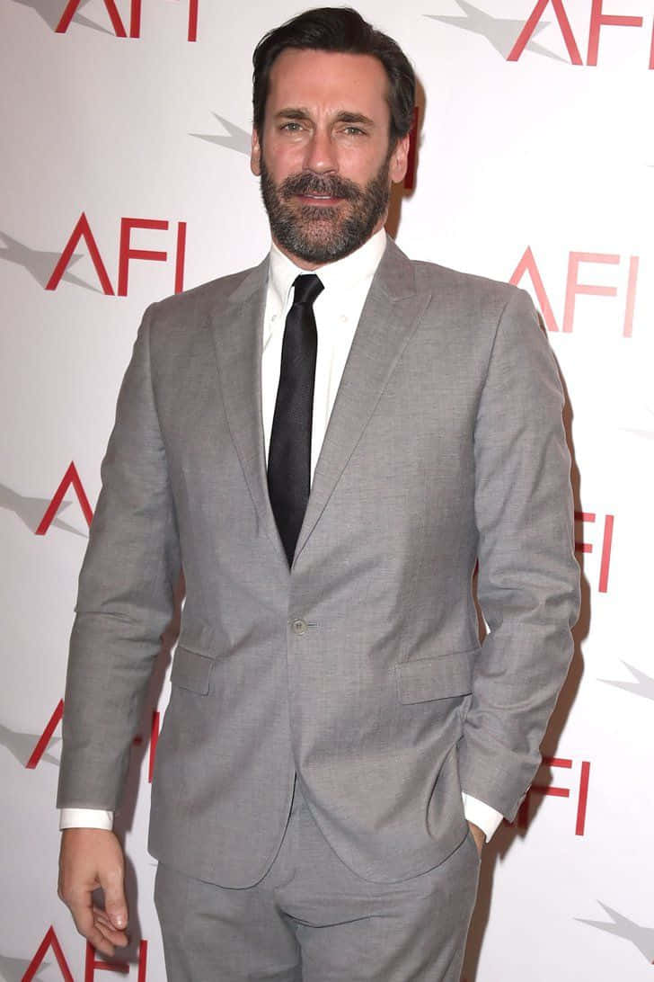 Jon Hamm 桌布 壁紙 — 一位留鬍鬚的男子穿著灰色西裝和黑色領帶，站在有紅色AFI標誌的白牆前。
