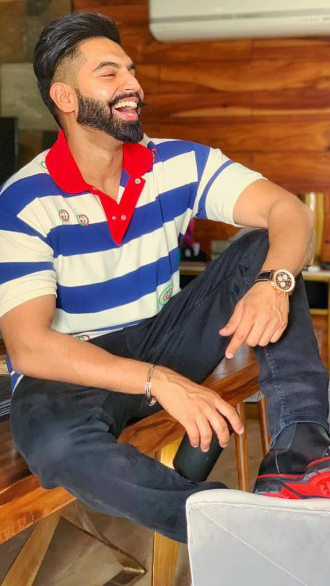 Indian 桌布 壁紙 — 一位留鬍鬚的男子穿著藍白條紋Polo衫，在室內木椅上輕鬆地開懷大笑。