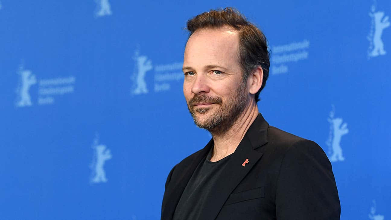 Peter Sarsgaard 桌布 壁紙 — 一位留鬍鬚的男子身穿深色西裝，自信地站在帶有柏林國際電影節標誌的藍色背景前。
