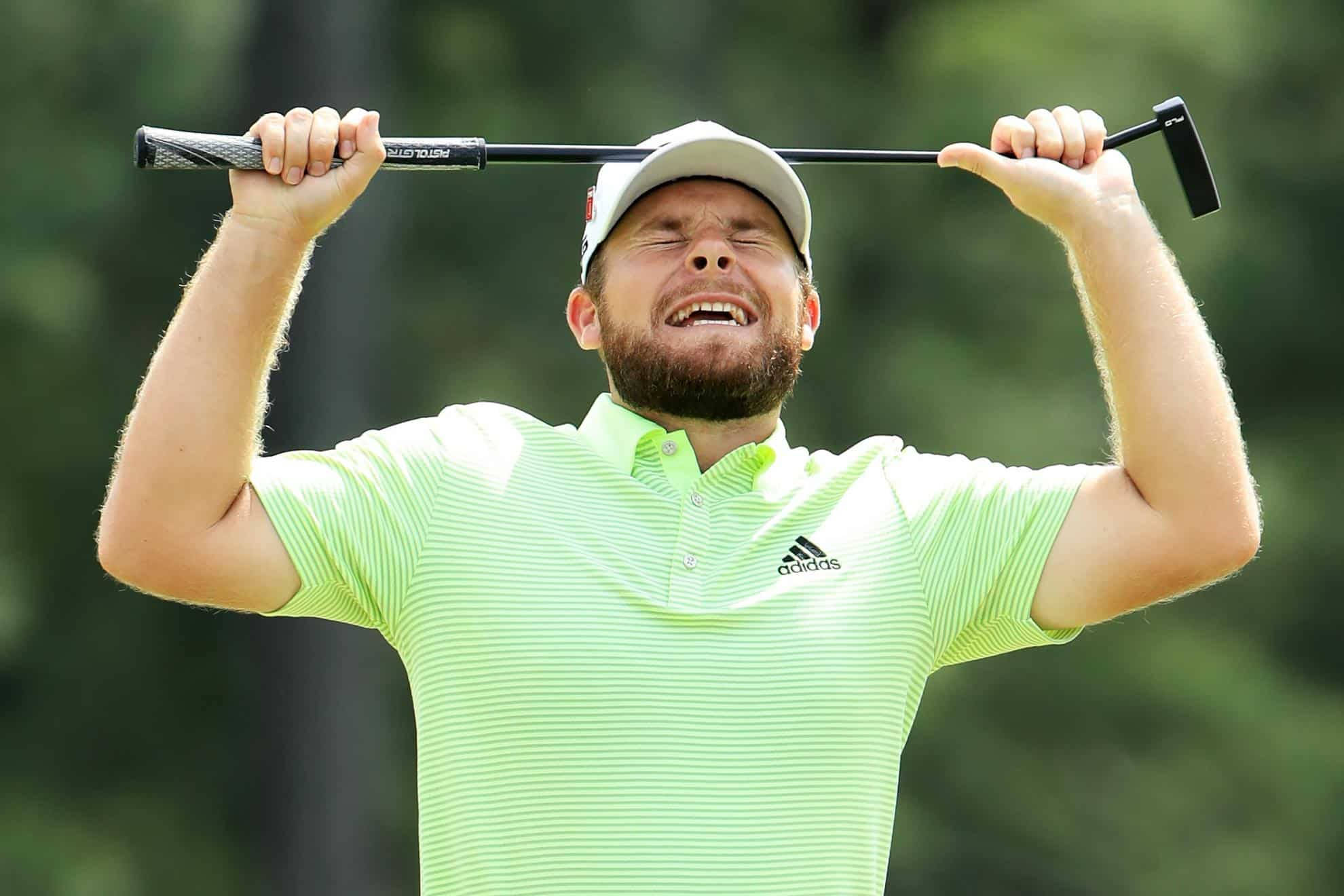 Tyrrell Hatton 桌布 壁紙 — 一位留鬍鬚的高爾夫球手身穿螢光綠色襯衫，在翠綠的球場上高舉推桿，開懷大笑。