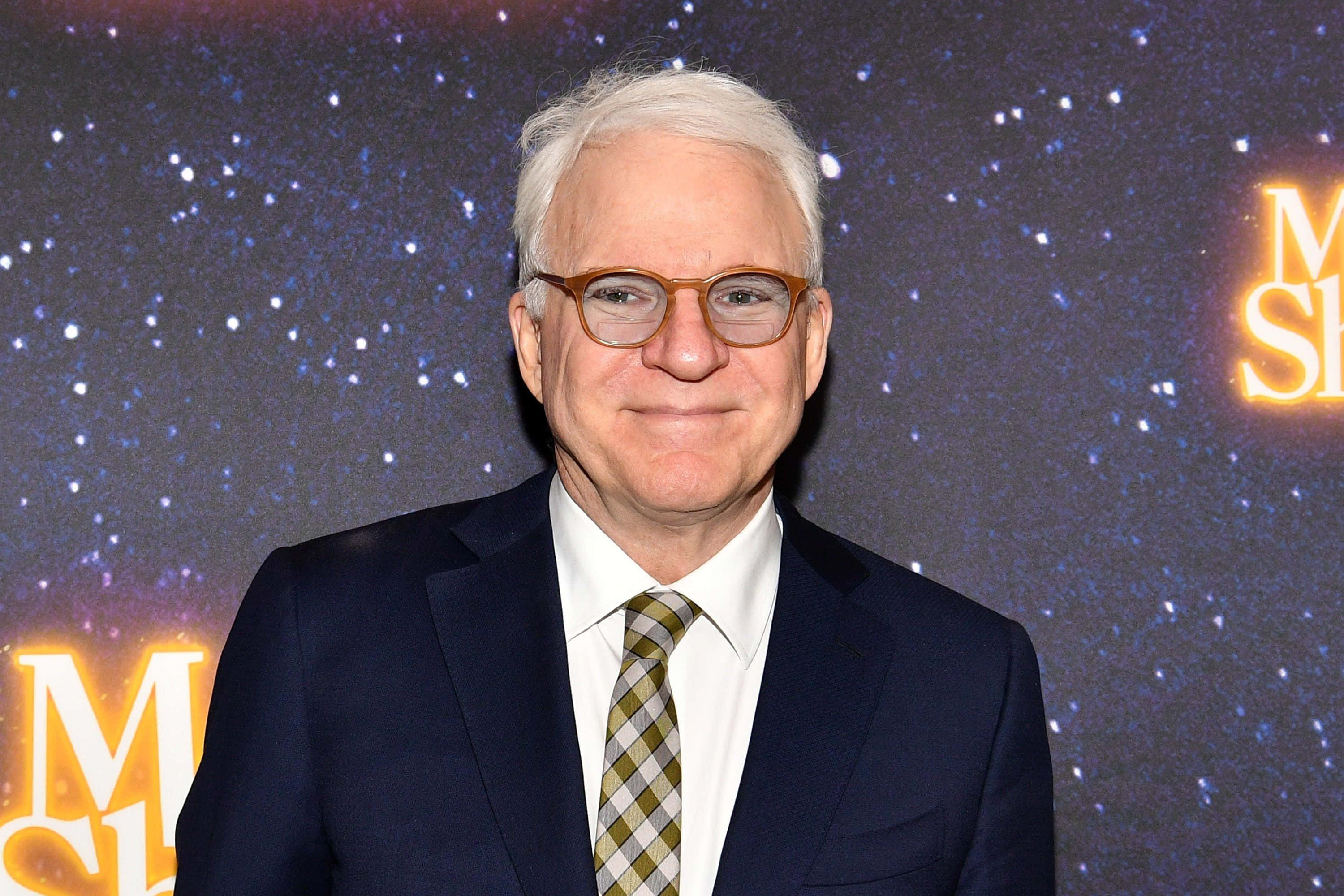 steve martin 桌布 壁紙 — 一位白髮戴眼鏡的男子穿著深色西裝，在星空背景下微笑，並有發光文字。