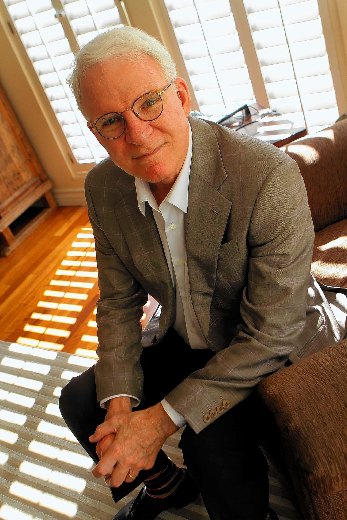 steve martin 桌布 壁紙 — 一位白髮戴眼鏡的長者坐在梳化上，房間陽光充足，木地板和百葉窗投射出條紋狀陰影。