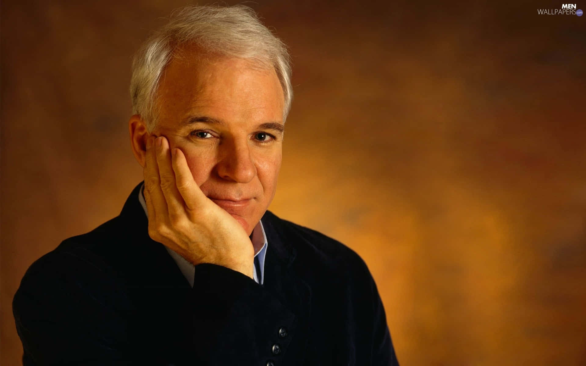steve martin 桌布 壁紙 — 一位白髮沉思的男子，在溫暖的漸變背景前，用手托著下巴。