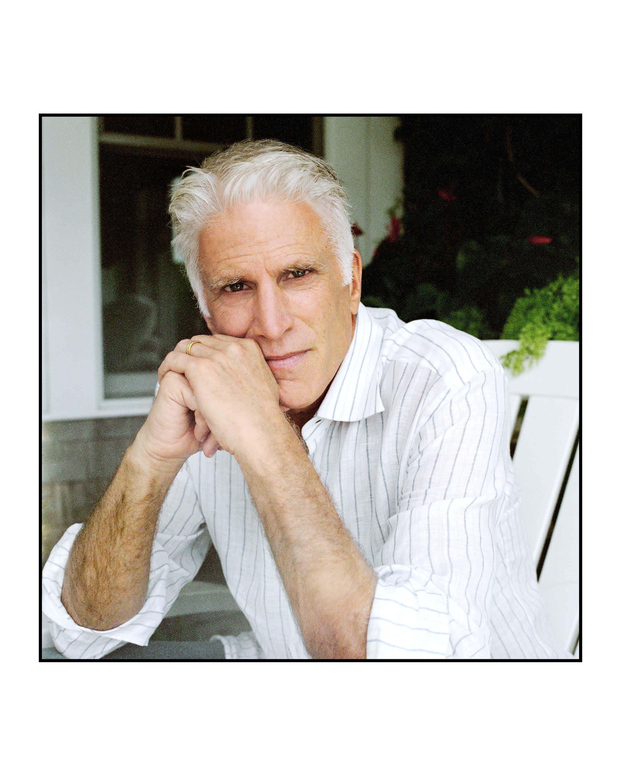 Ted Danson 桌布 壁紙 — 一位白髮的成熟男士，穿著條紋襯衫坐在戶外，雙手交疊托著下巴。