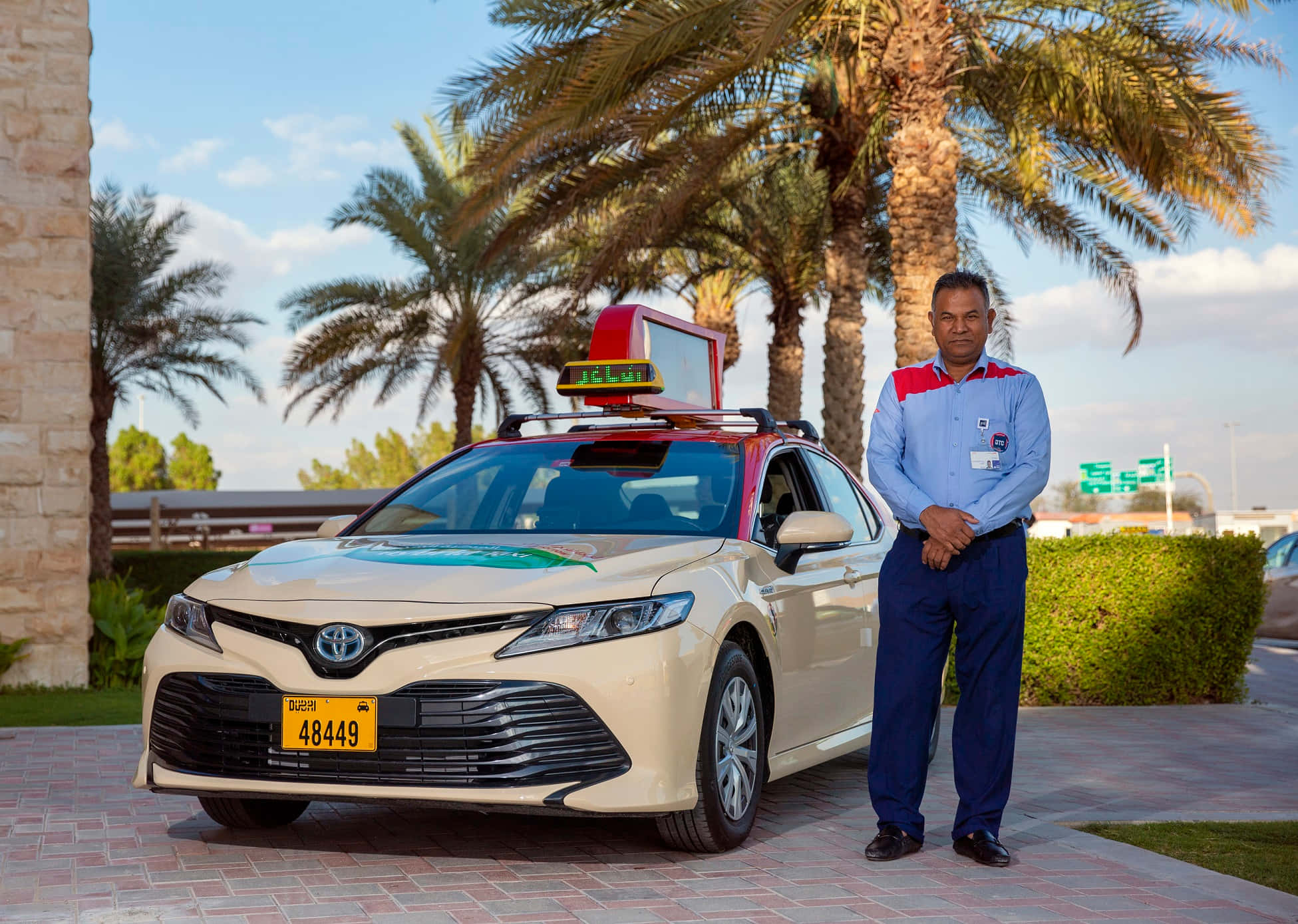 taxi 桌布 壁紙 — 一位的士司機在陽光明媚的沙漠環境中，自豪地站在棕櫚樹下他的奶油色豐田Camry的士旁邊。