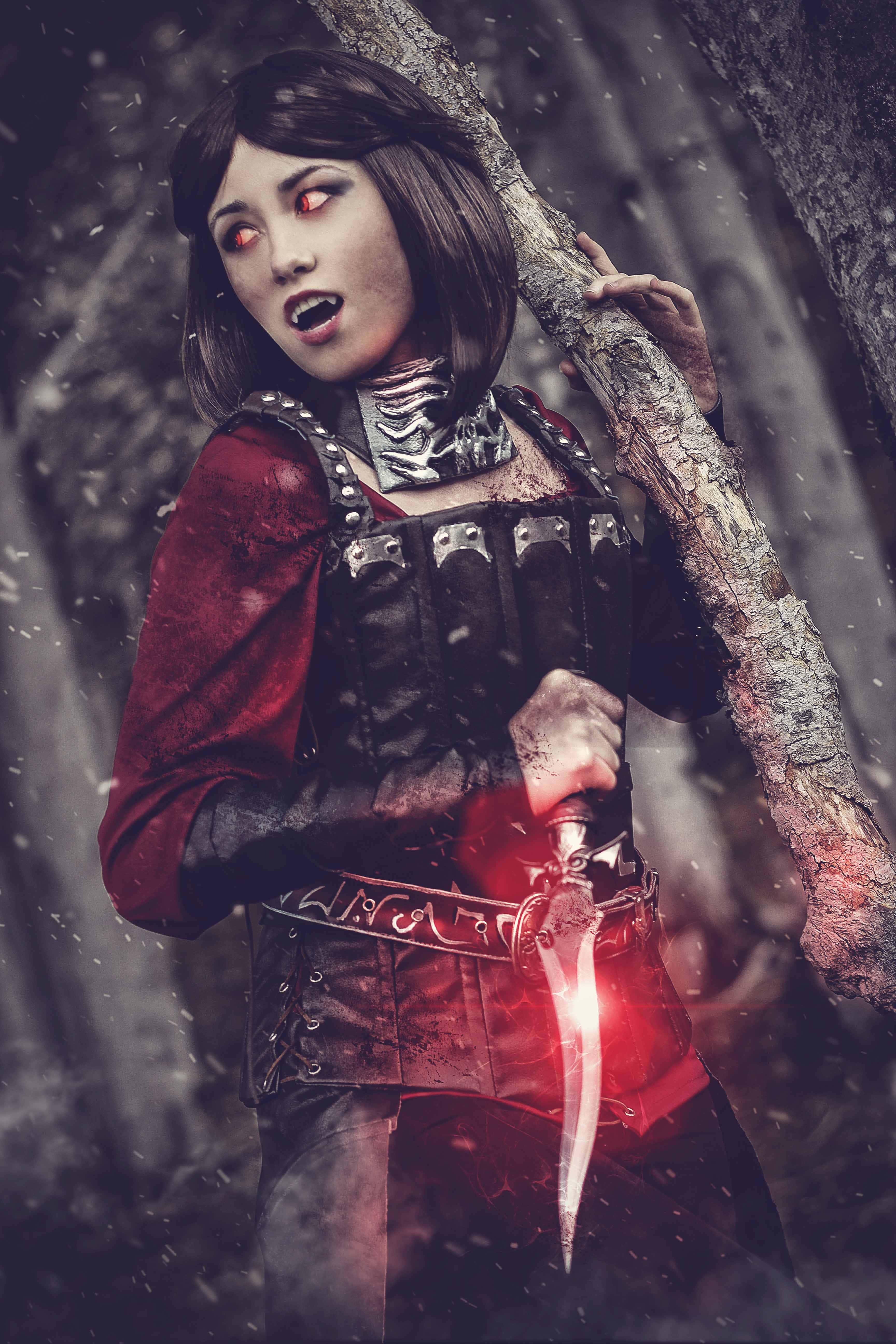 Skyrim Serana 桌布 壁紙 — 一位眼神兇猛、雙眼發出紅光的女戰士，在白雪覆蓋的森林中緊握著一把發光的匕首和樹枝。