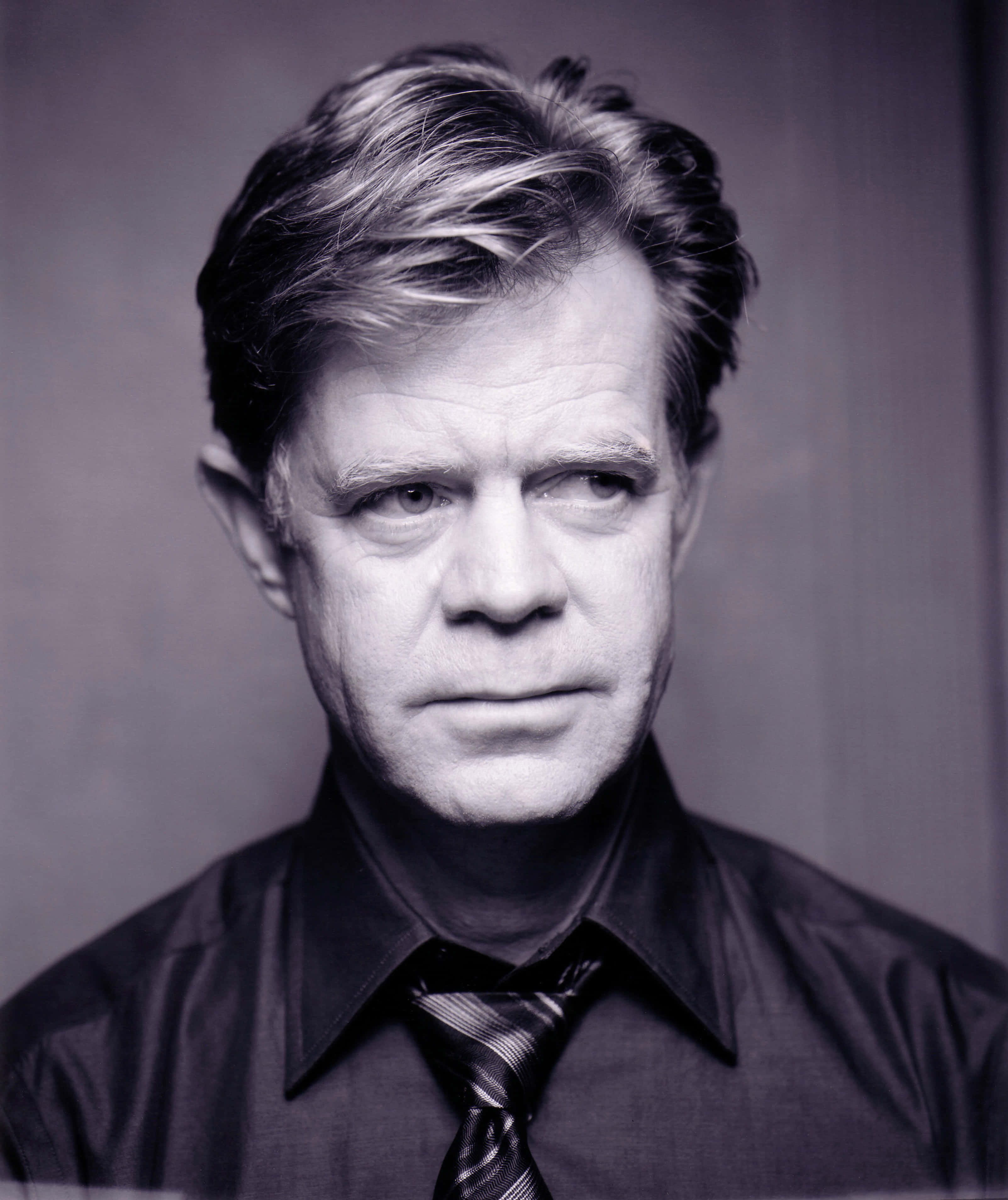 william h. macy 桌布 壁紙 — 一位眼神銳利、頭髮有紋理的男士黑白肖像，穿著有領襯衫和條紋領帶。