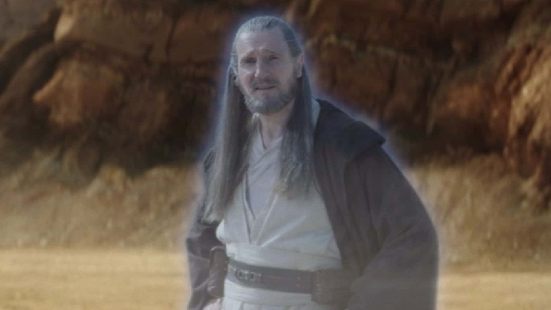 Qui-gon Jinn 桌布 壁紙 — 一位睿智、飄逸的長者，長長灰髮和鬍鬚，站在沙漠峽谷中，在崎嶇的岩層間柔和發光。
