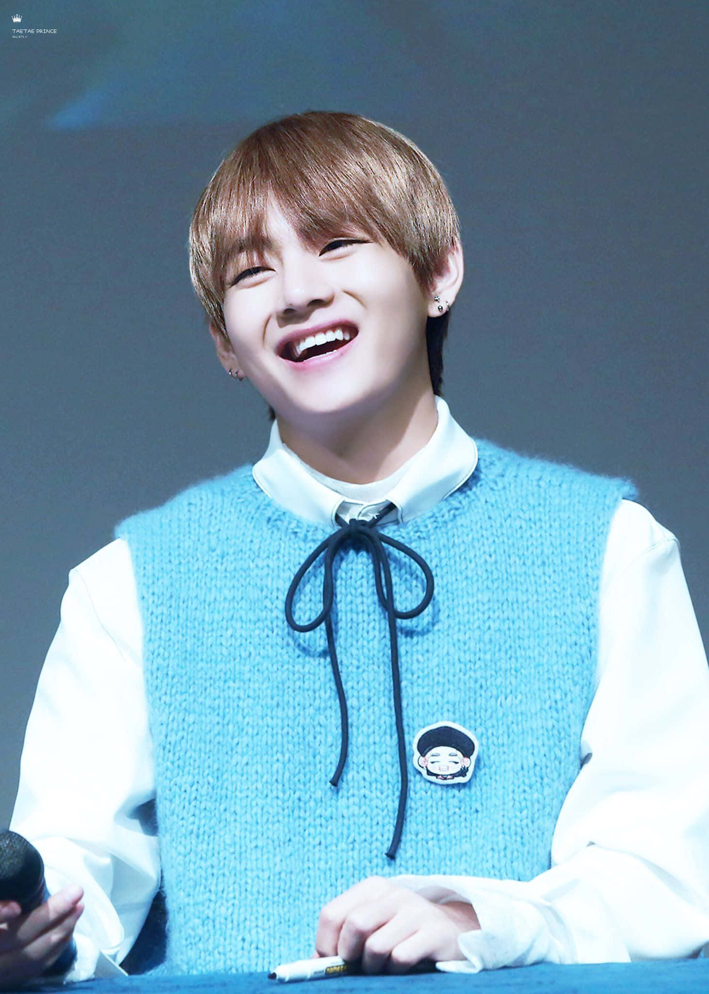 Taehyung Cute 桌布 壁紙 — 一位短棕髮的年輕男子在簽名活動中，穿著淺藍色針織背心內搭白襯衫，開懷大笑。