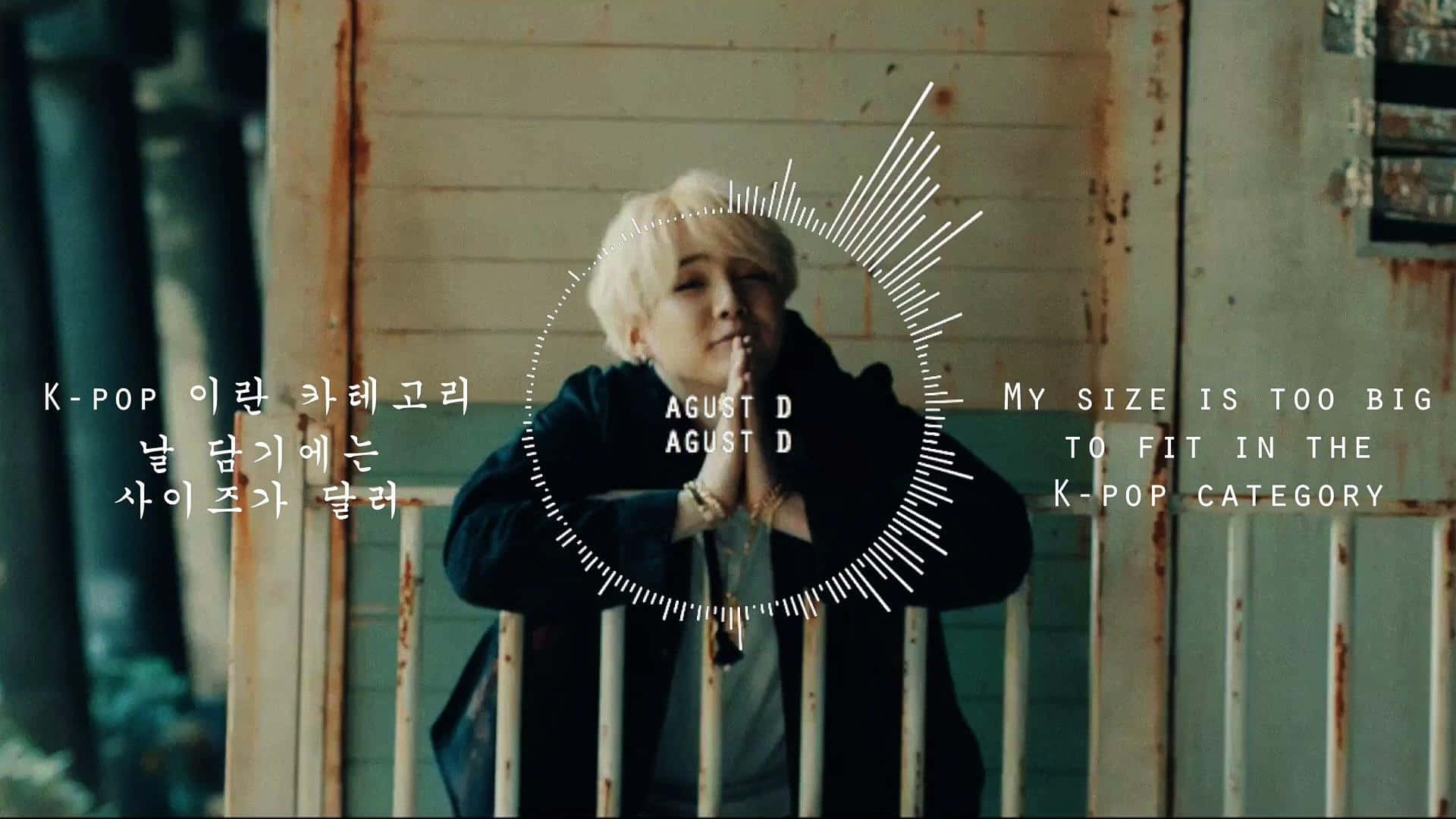 Agust D 桌布 壁紙 — 一位短白金髮的人站在生鏽的金屬欄杆後面，處於昏暗的工業環境中，帶有韓文和英文的文字疊加。
