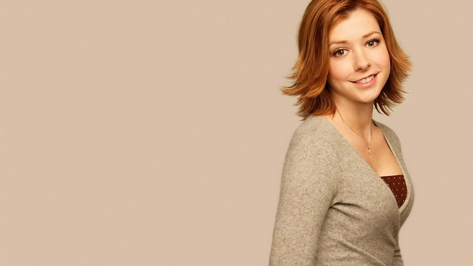 Alyson Hannigan 桌布 壁紙 — 一位短紅髮的女性穿著灰色開襟毛衣，在純米色背景前溫暖地微笑。