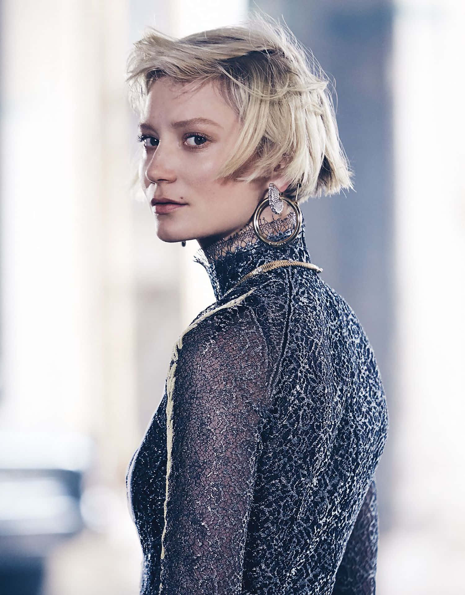 Mia Wasikowska 桌布 壁紙 — 一位短金髮、戴大圈耳環的女性，穿著黑色蕾絲上衣，轉頭越過肩膀。