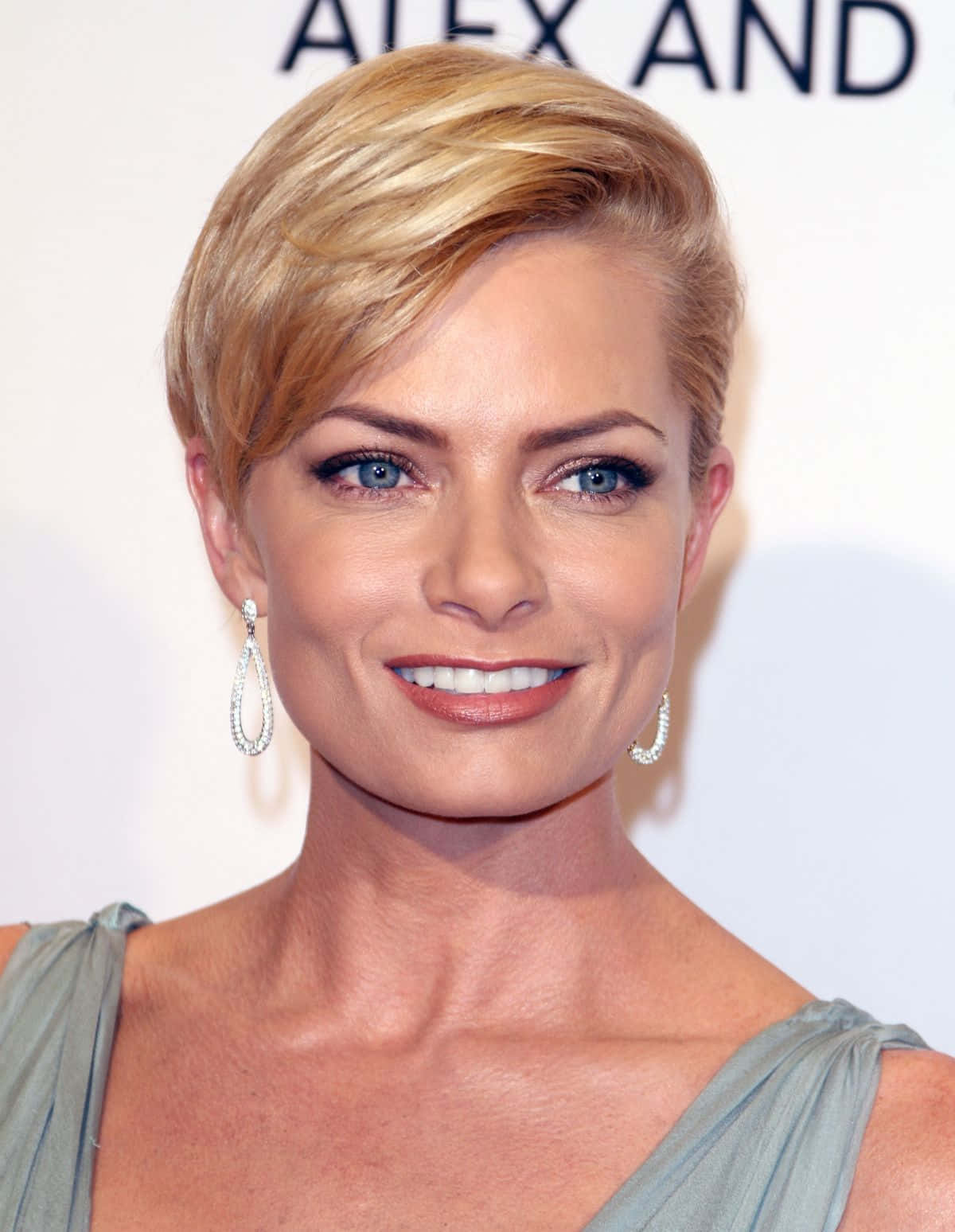 Jaime Pressly 桌布 壁紙 — 一位短金髮藍眼女士戴著優雅耳環微笑面向鏡頭的近距離肖像。