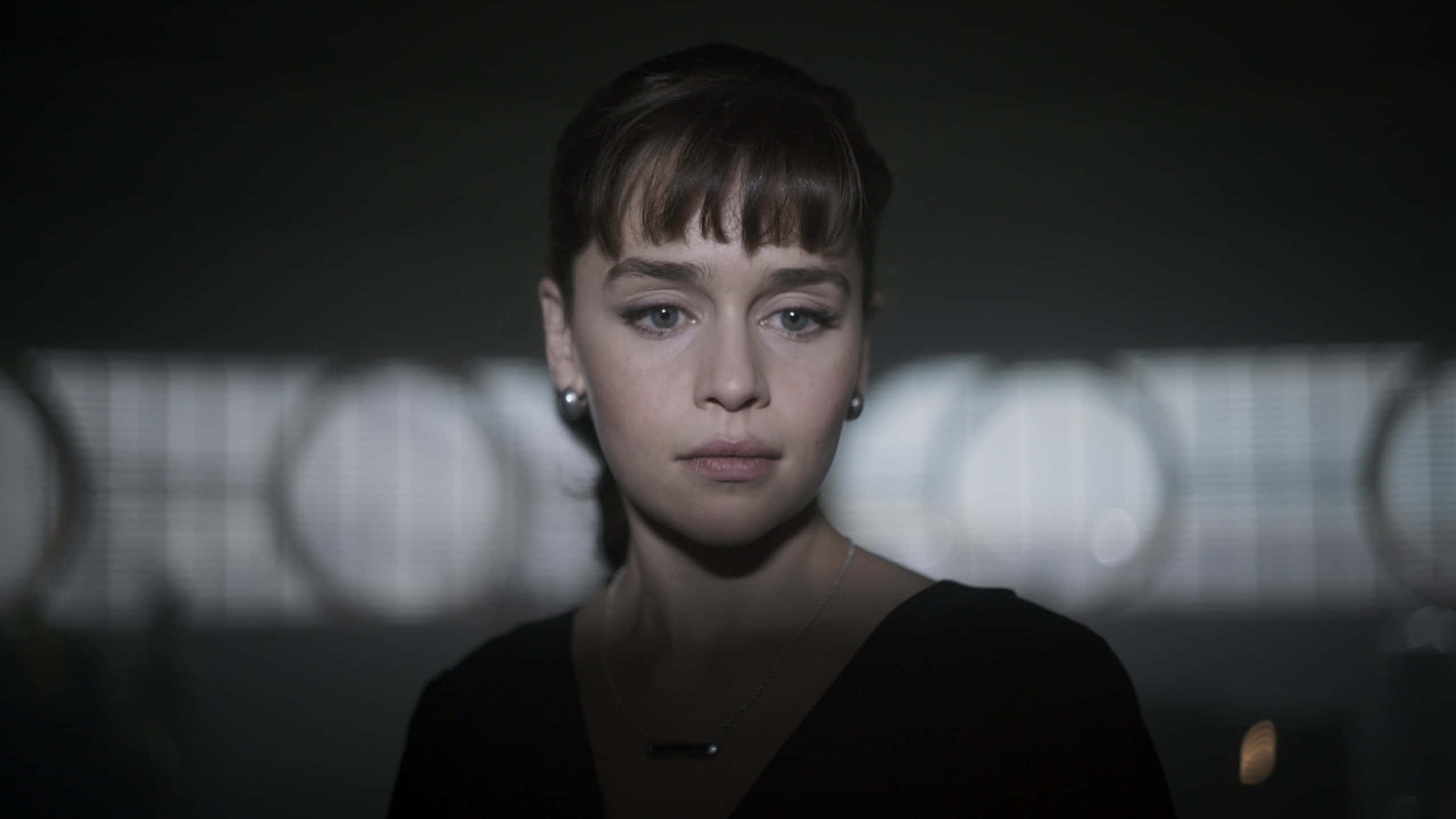 Solo A Star Wars Story 桌布 壁紙 — 一位短黑髮、眼神銳利的女性在昏暗的房間中向前凝視，身後有模糊的圓形燈光。