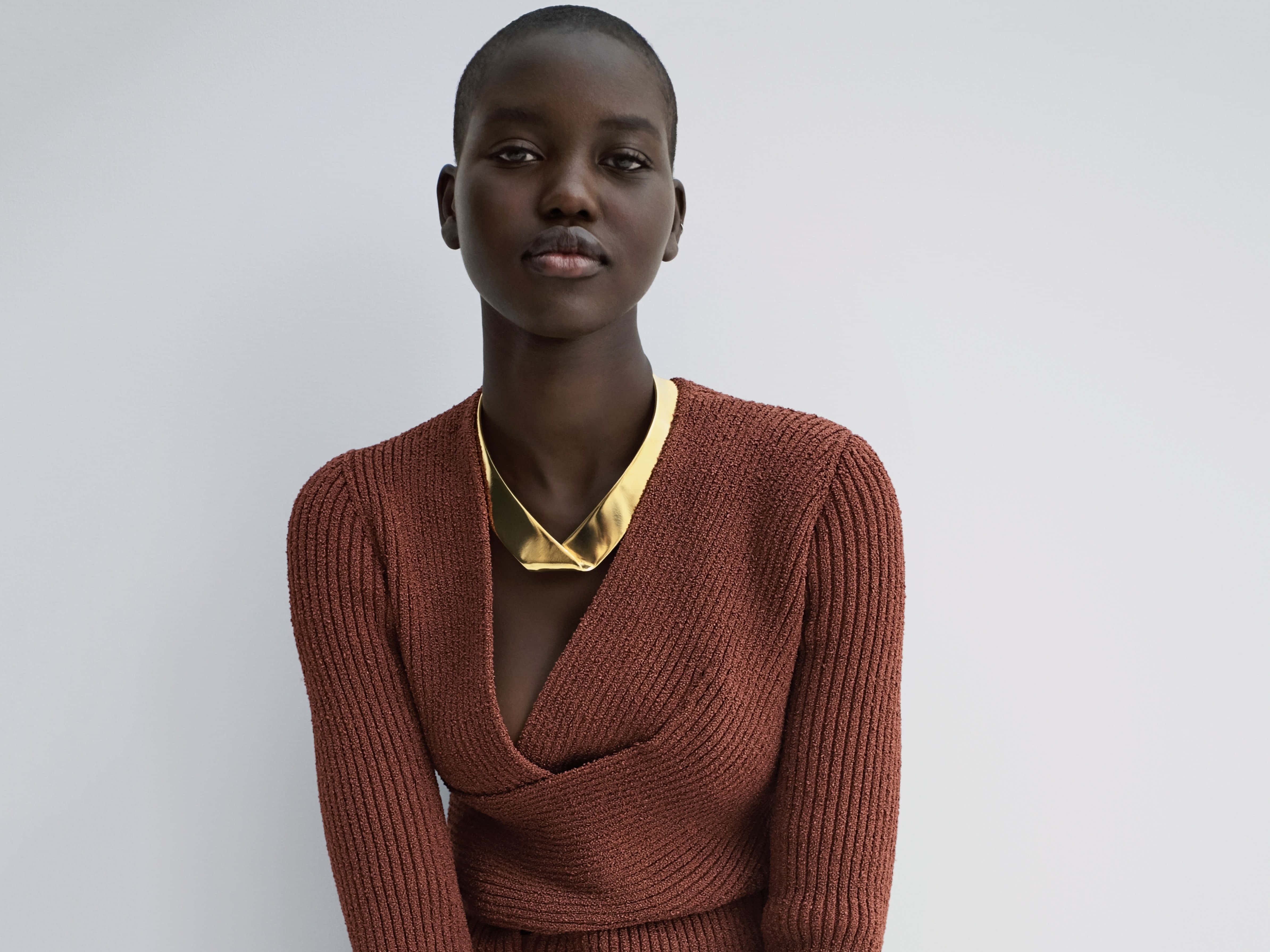 Minimalist Fashion 桌布 壁紙 — 一位短黑髮的優雅女性，在純白背景前穿著鏽紅色羅紋毛衣和搶眼的金色頸鏈。