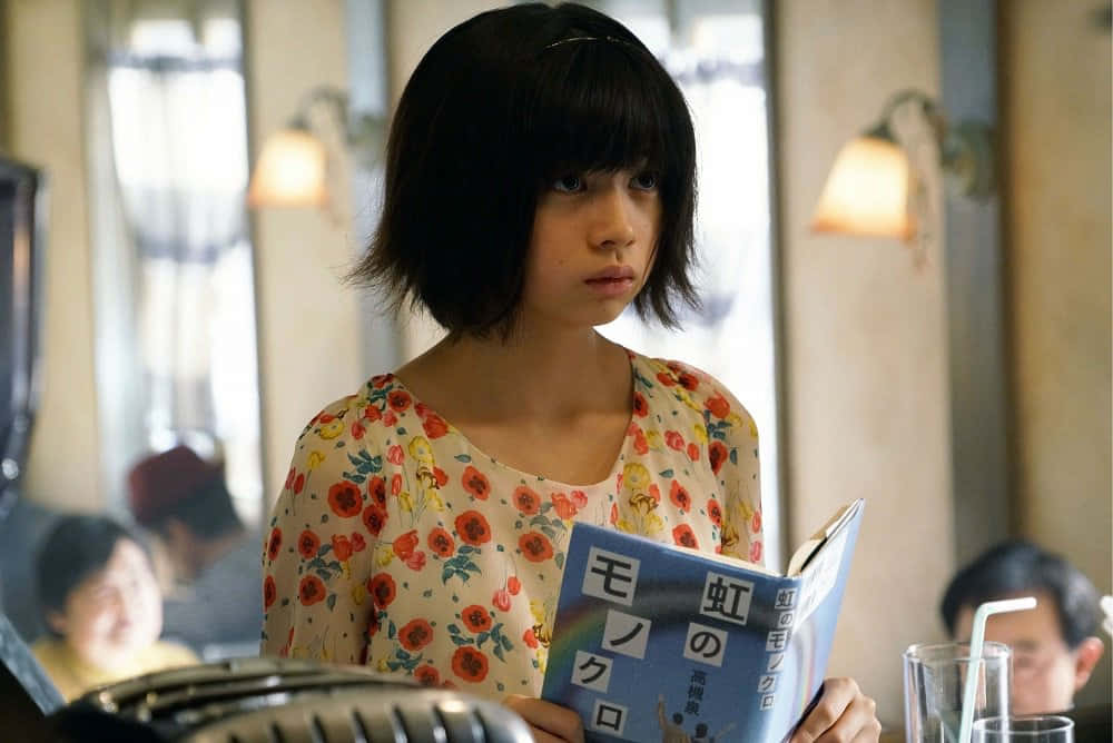 Tokyo Ghoul Movie 桌布 壁紙 — 一位短黑髮的年輕女性在燈光溫暖的咖啡館裡看書，背景柔和模糊。