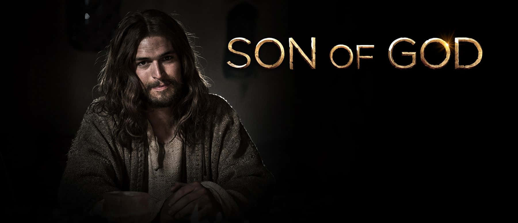 Son Of God 桌布 壁紙 — 一位神情肅穆、長髮鬍鬚的男子在昏暗光線中凝視前方，旁邊有金色的「SON OF GOD」文字。