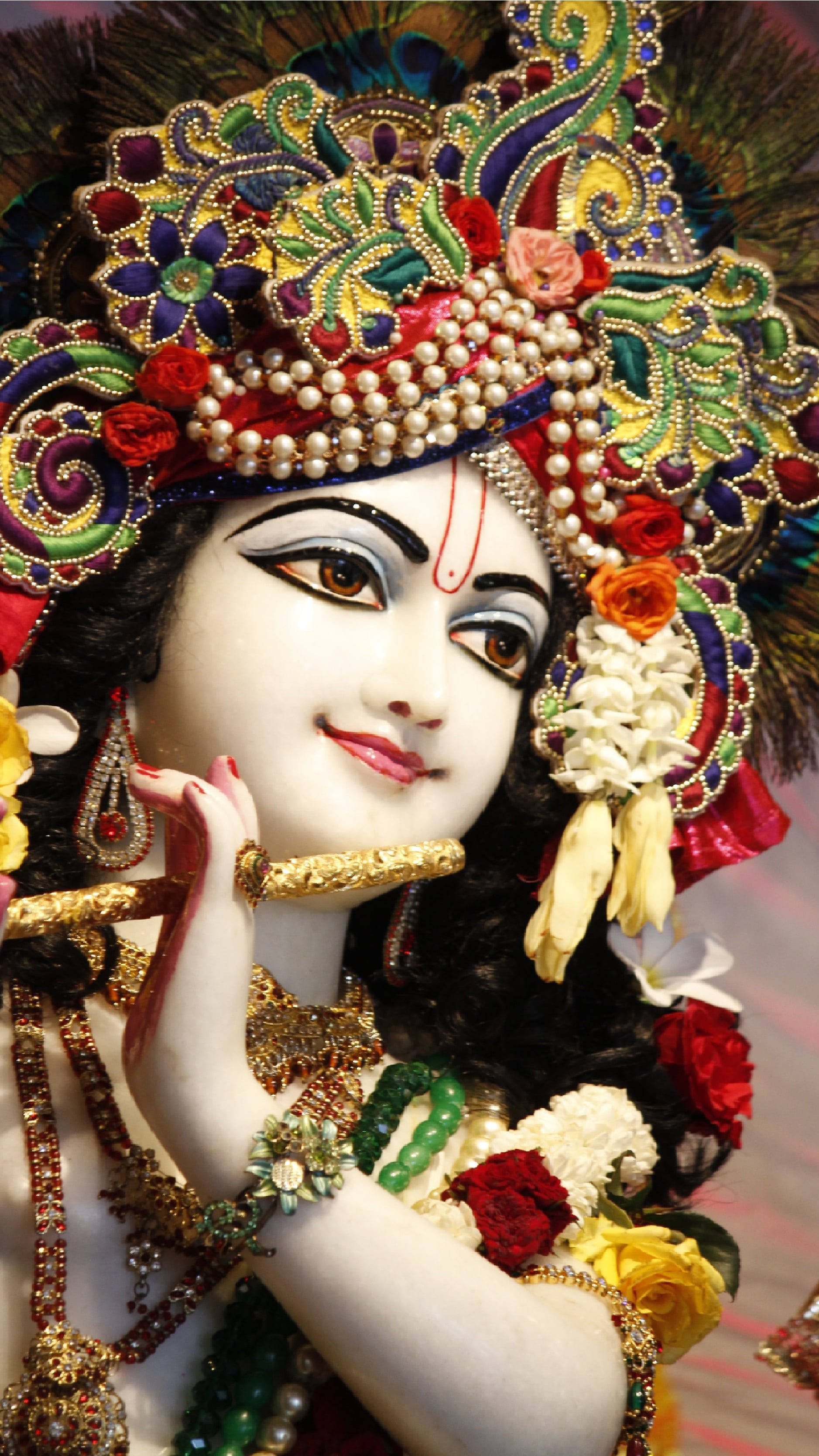 krishna phone 桌布 壁紙 — 一位神聖人物裝飾著鮮豔的寶石、花朵和孔雀羽毛，以寧靜的優雅手持長笛。