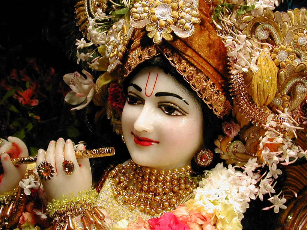 krishna god 桌布 壁紙 — 一位神聖的人物，佩戴金色珠寶和花冠，在深色花卉背景下優雅地吹奏長笛。