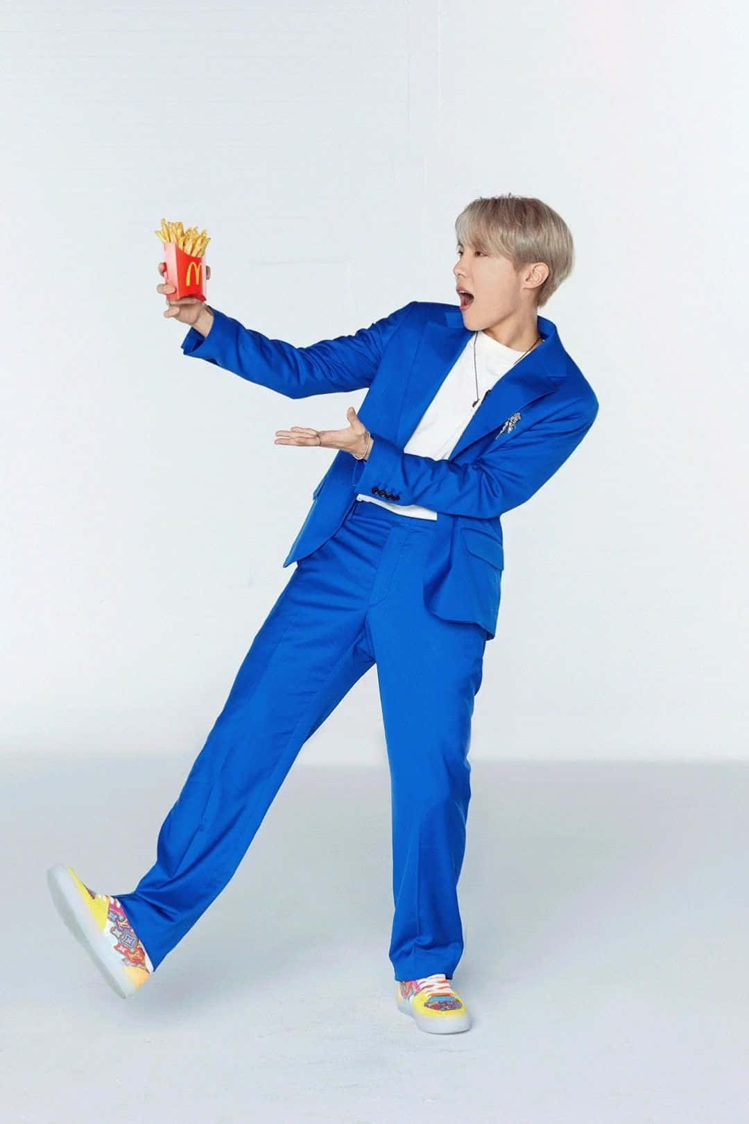 Bts Endorsements 桌布 壁紙 — 一位穿著亮藍色西裝的年輕男子，在純白色工作室背景前俏皮地拿著麥當勞薯條盒。