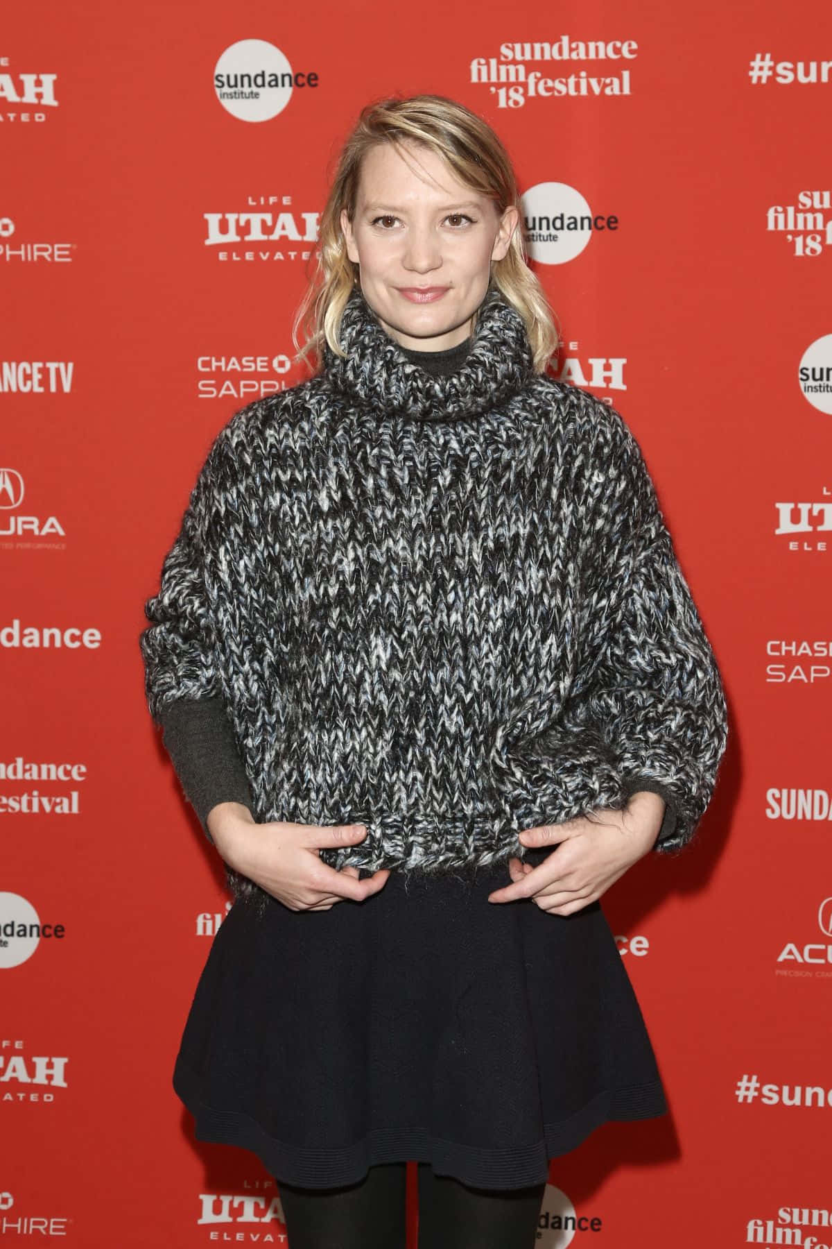 Mia Wasikowska 桌布 壁紙 — 一位穿著厚實黑白針織毛衣的女性自信地站在鮮紅色的辛丹斯電影節背景前。