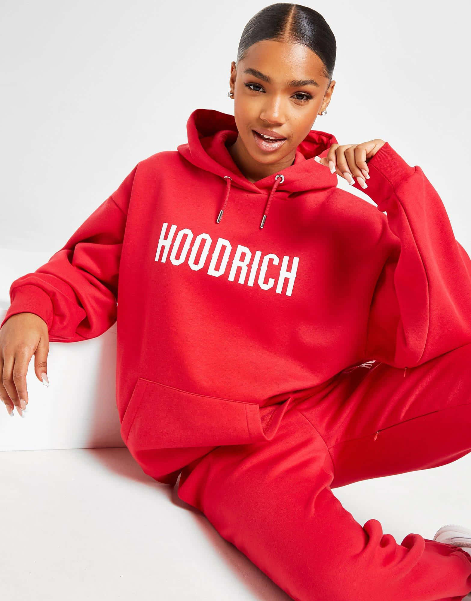 Red Hoodie 桌布 壁紙 — 一位穿著大膽紅色連帽衫、帶有白色 'HOODRICH' 字樣的女性，隨意地坐在白色背景前。