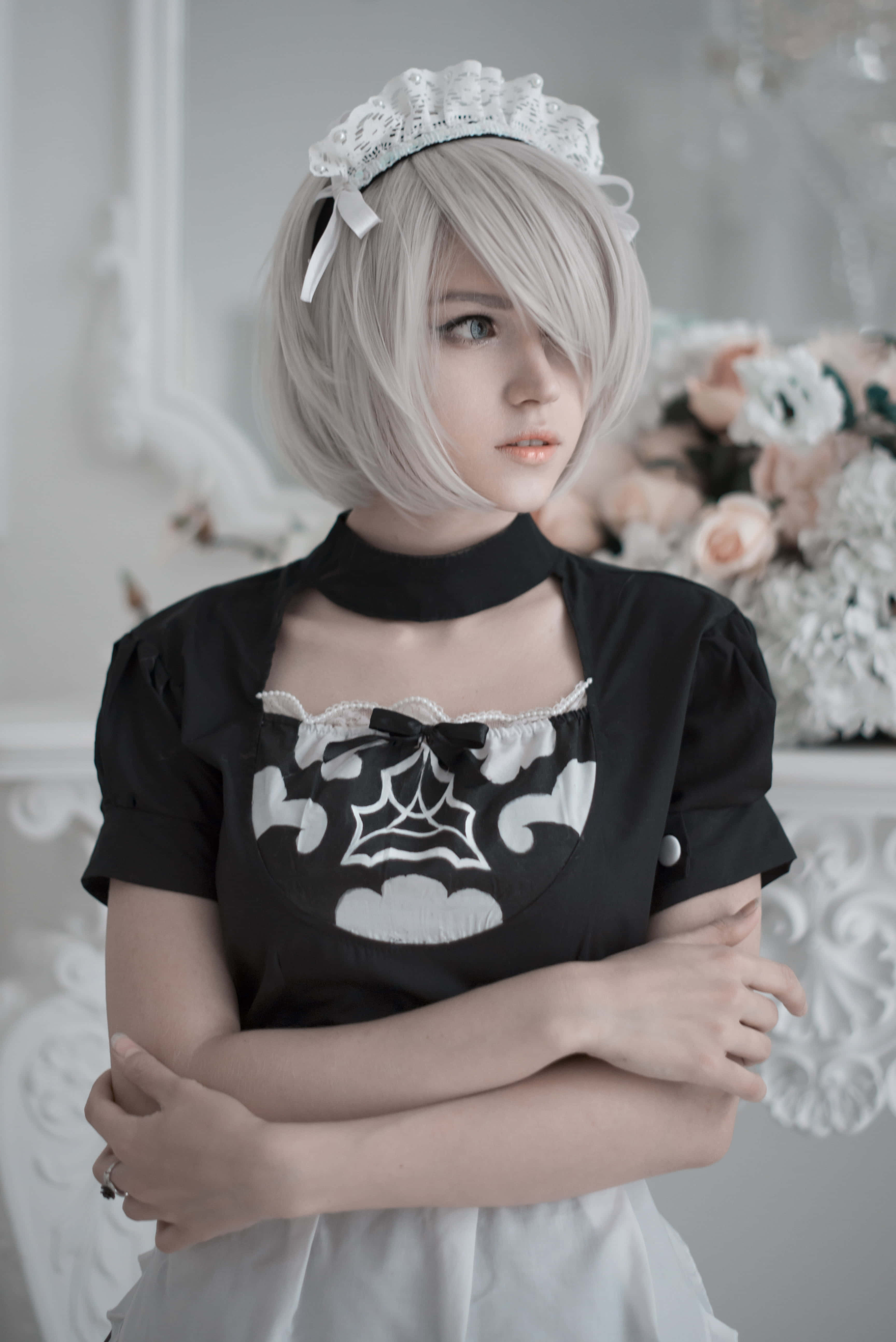 Gaming Cosplay 桌布 壁紙 — 一位穿著女僕裝、銀色頭髮和蕾絲頭飾的人，在柔和光線的華麗房間中交叉雙臂站立。