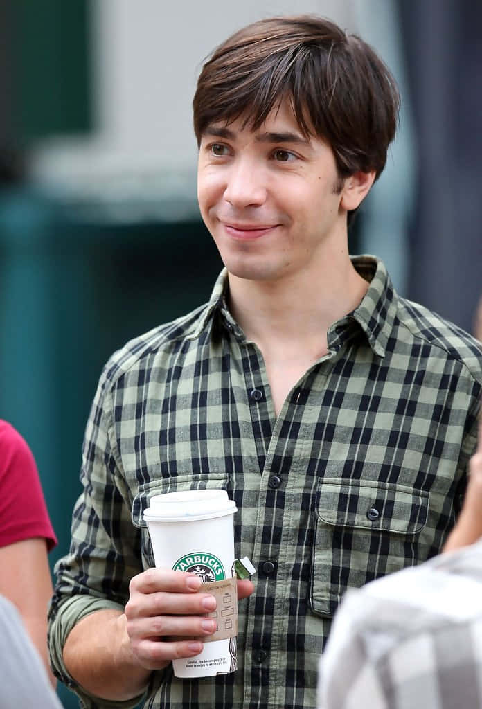 Justin Long 桌布 壁紙 — 一位穿著格仔恤衫的年輕男士，喺戶外手持Starbucks咖啡杯微笑。
