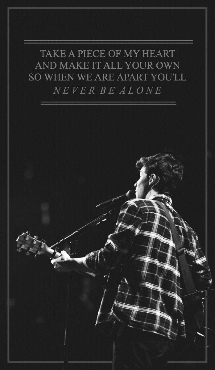 Shawn Mendes《Never Be Alone》 壁紙 — 一位穿著格仔恤衫的音樂家在昏暗燈光下在舞台上彈結他，並疊加了浪漫的歌詞。