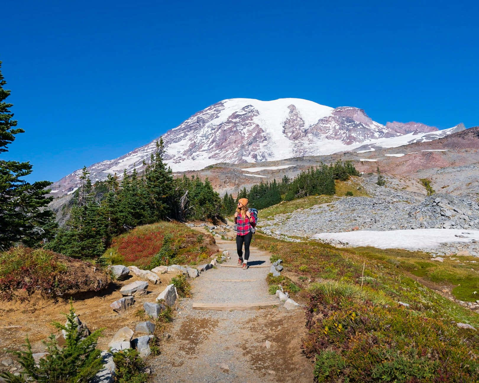 Hiking 桌布 壁紙 — 一位穿著格仔衫的遠足者沿著石徑走向一座白雪覆蓋的山峰，天空清澈湛藍。