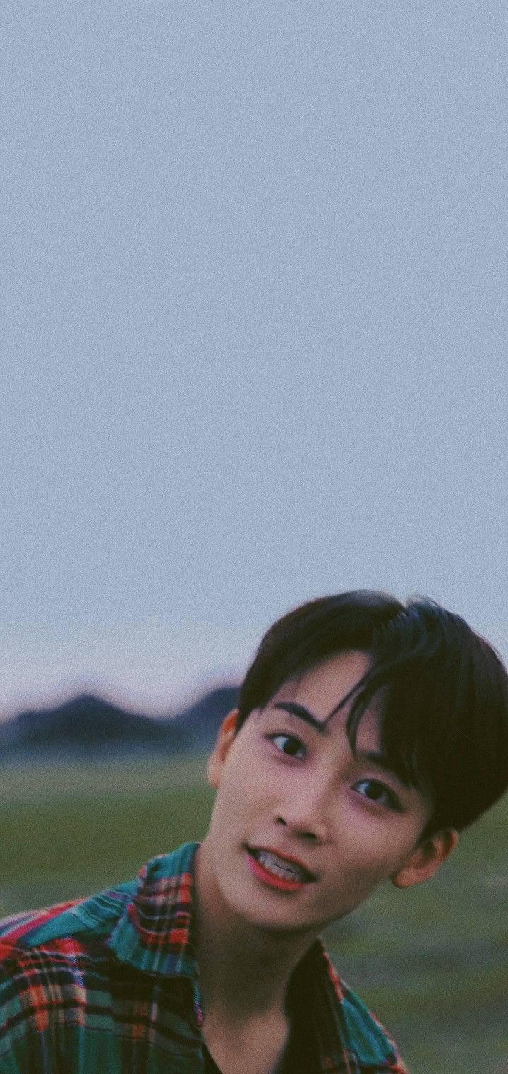 Yoon Jeonghan Snap Shoot 壁紙 — 一位穿著格仔襯衫的年輕男子在暮色山景背景下柔和地微笑，色調為柔和的藍色和綠色。