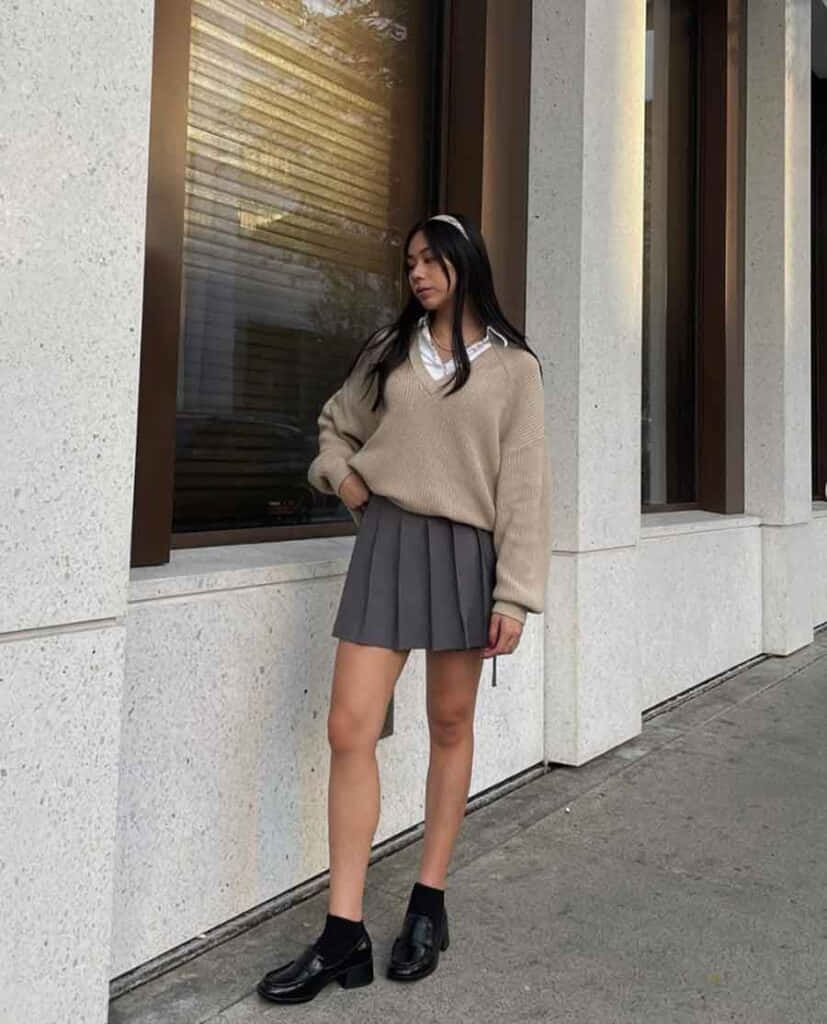 一位穿著毛衣和裙子的女士站在牆邊 壁紙