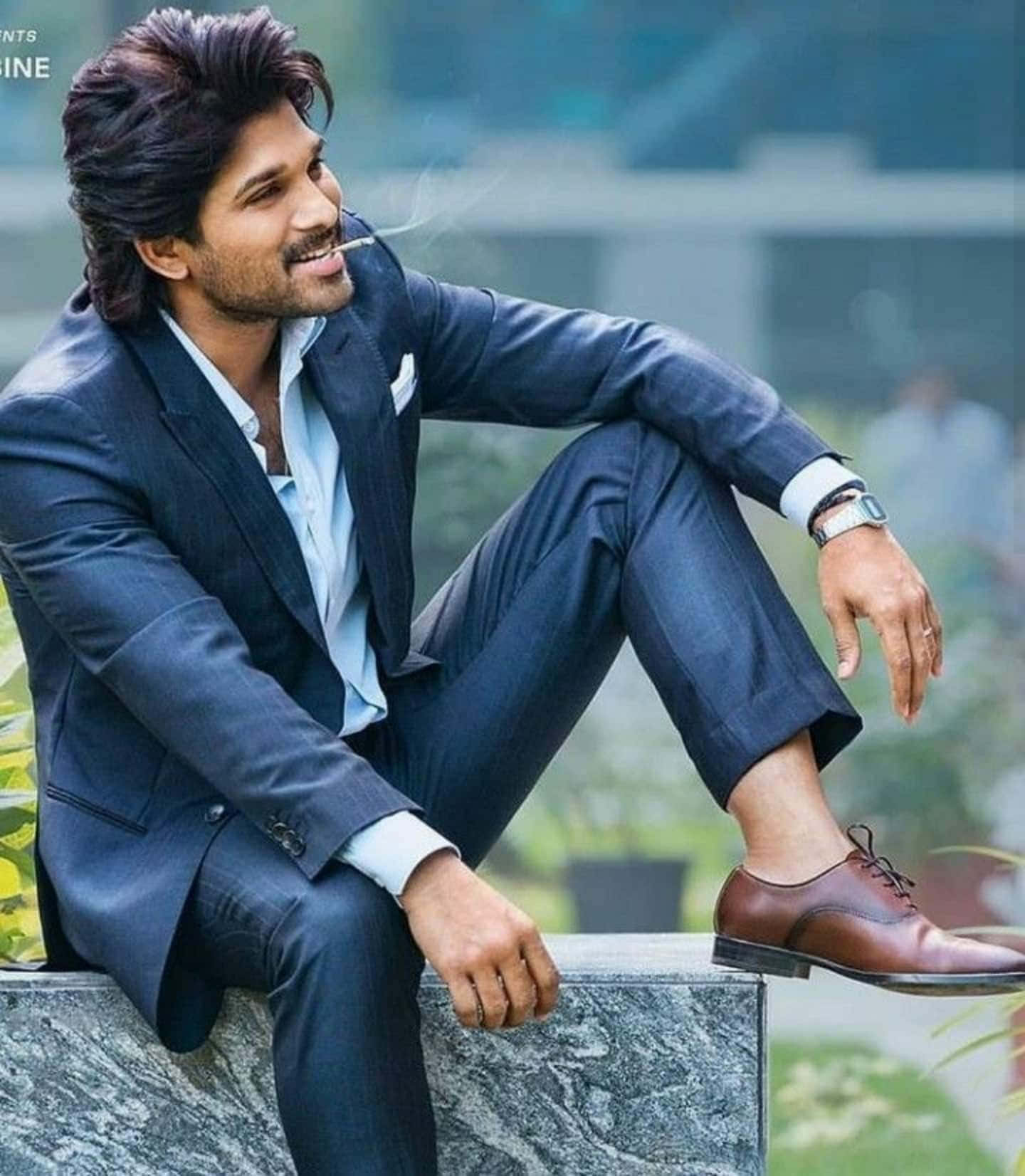 Allu Arjun 桌布 壁紙 — 一位穿著海軍藍西裝的時尚男士，隨意地坐在大理石邊緣，自信地微笑著抽煙。