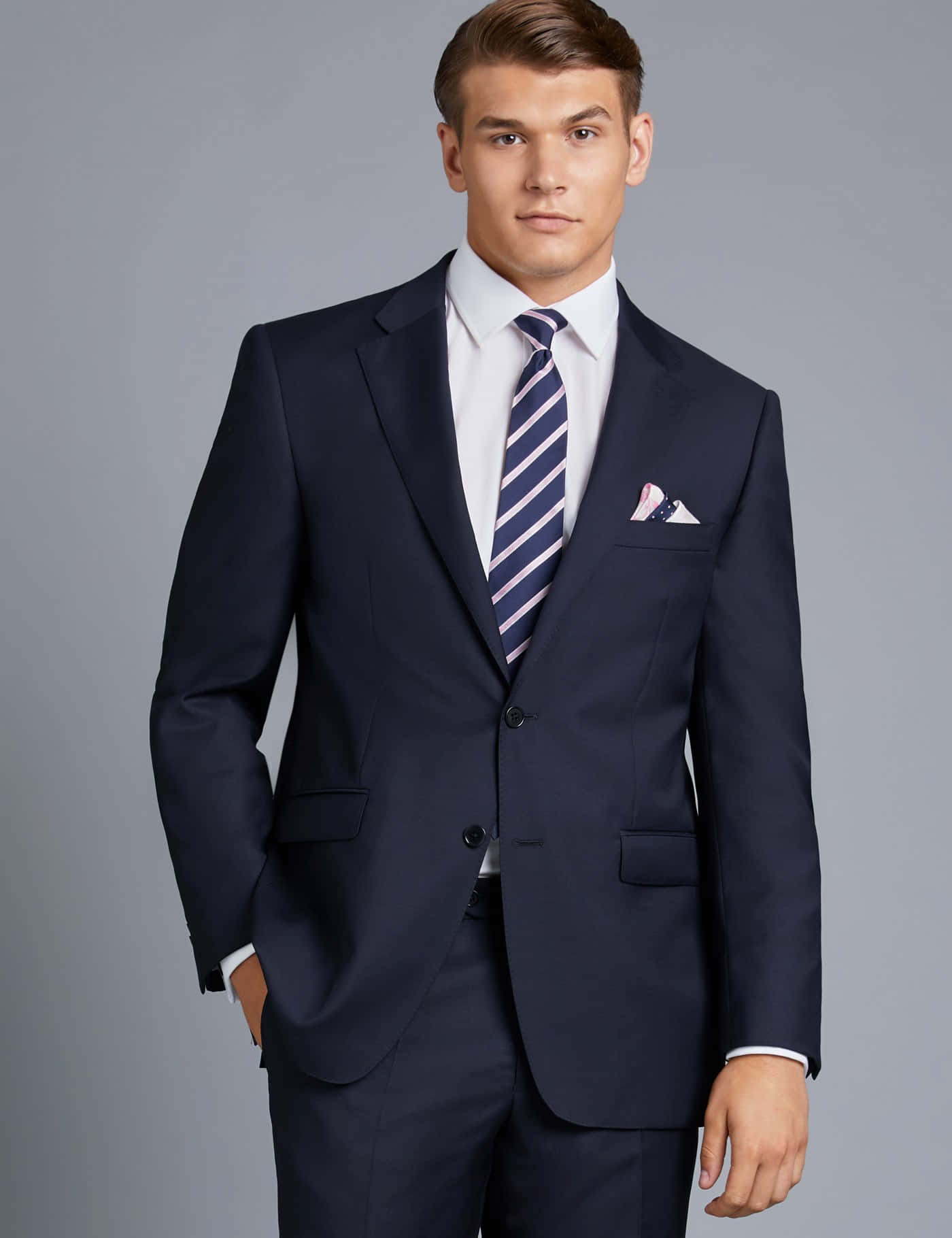 suit 桌布 壁紙 — 一位穿著海軍藍西裝配條紋領帶的時尚男士，自信地站在中性灰色背景前。