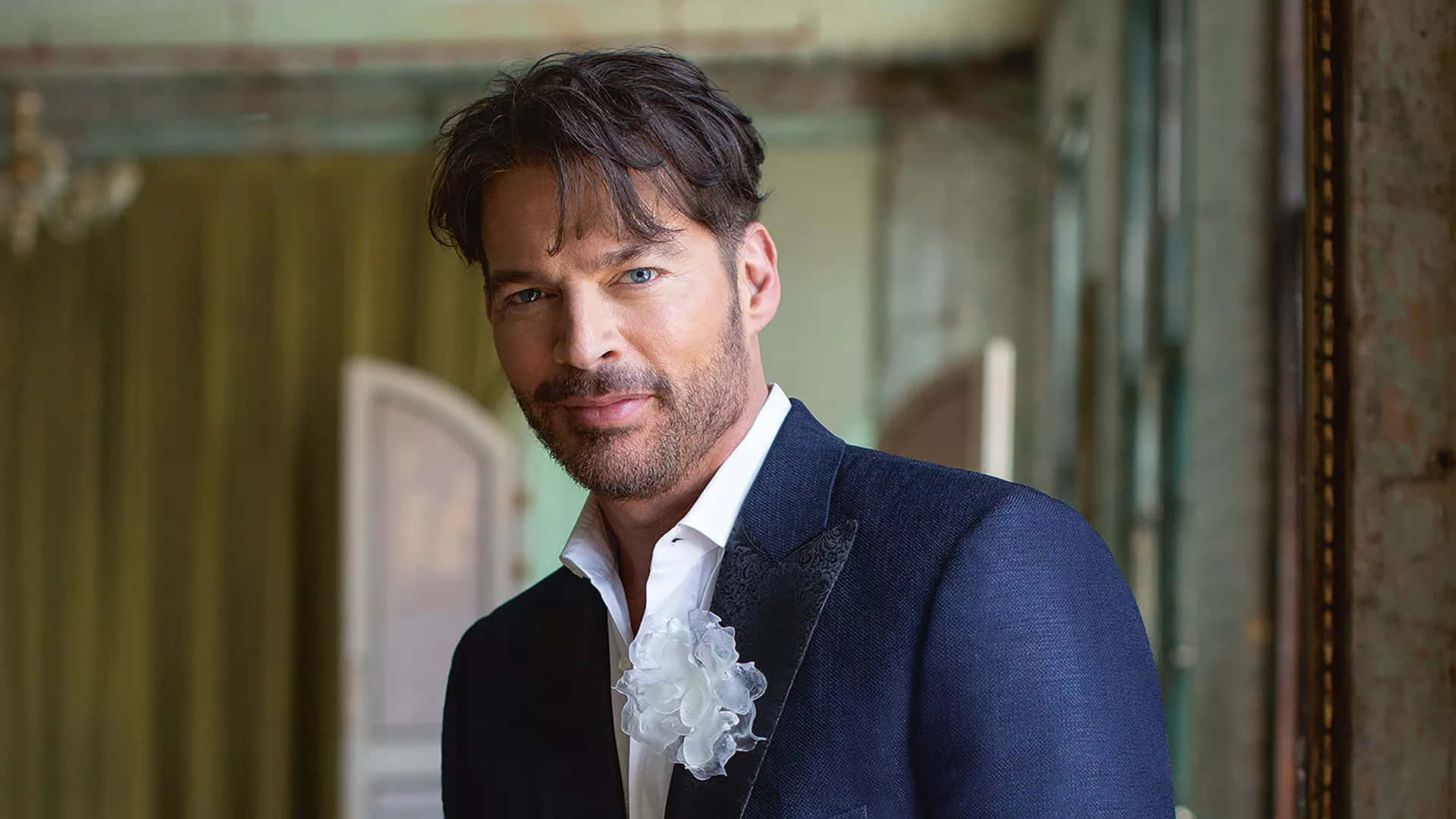 Harry Connick Jr 桌布 壁紙 — 一位穿著深色西裝、佩戴白色花卉胸花的英俊男子，自信地站在復古華麗的走廊中。