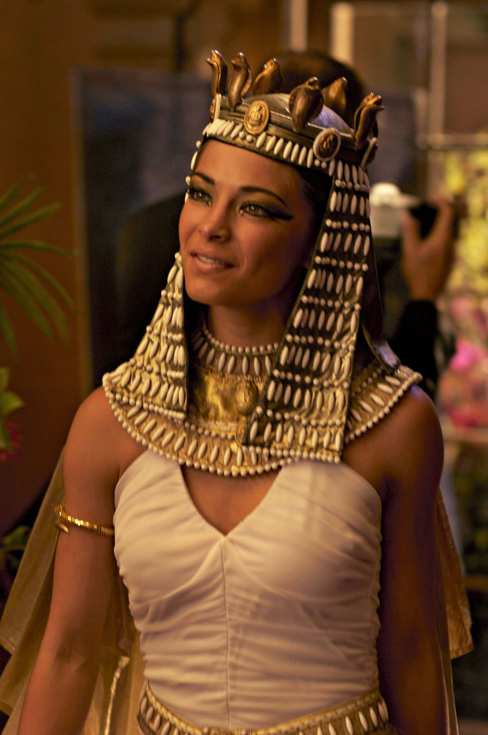 Cleopatra 桌布 壁紙 — 一位穿著精緻埃及女王服飾、戴著金冠和珠寶的女性對著鏡頭溫暖微笑。