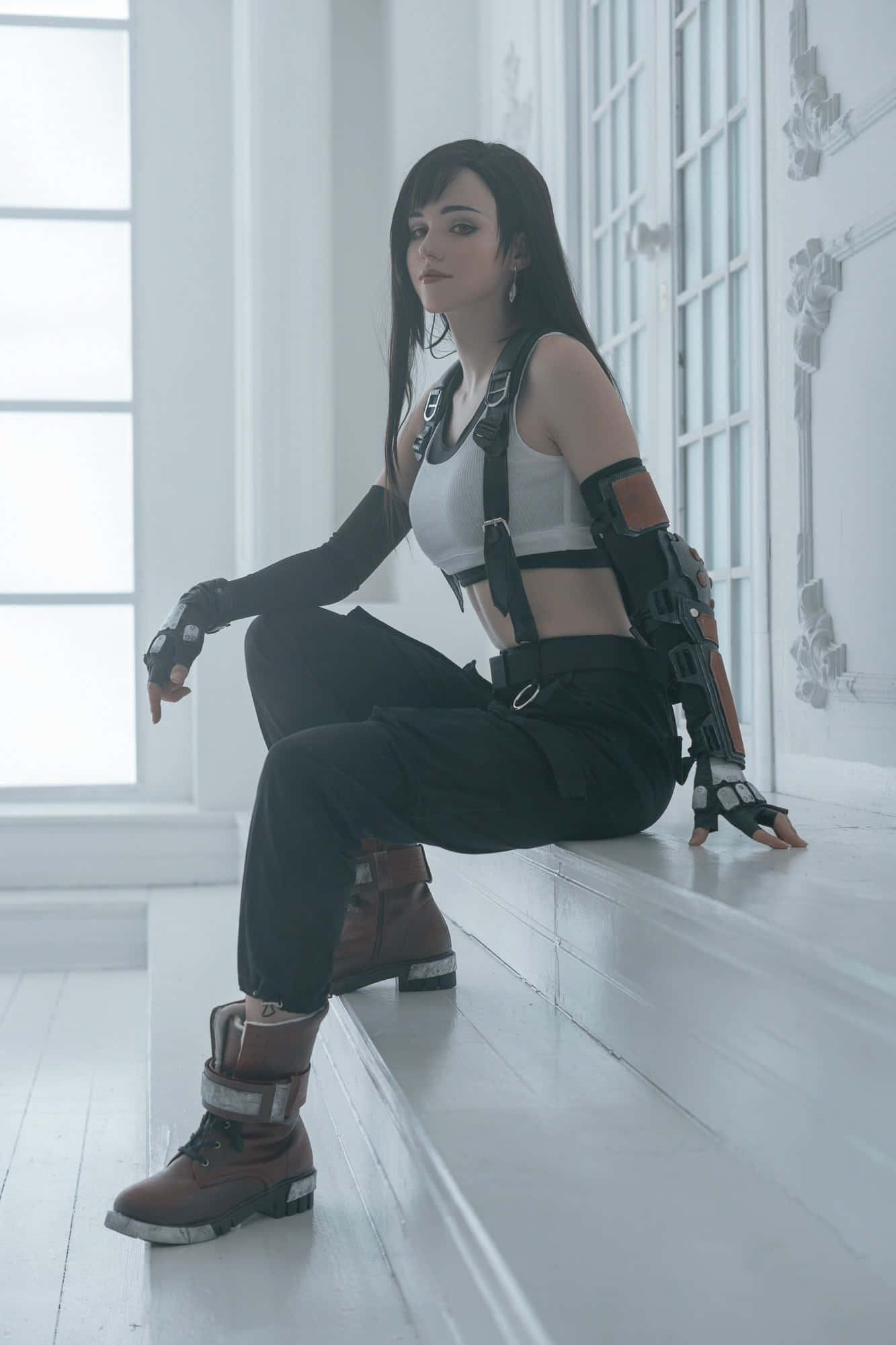 Gaming Cosplay 桌布 壁紙 — 一位穿著精緻黑白戰術服裝的角色扮演者，坐在明亮簡約房間的白色階梯上。