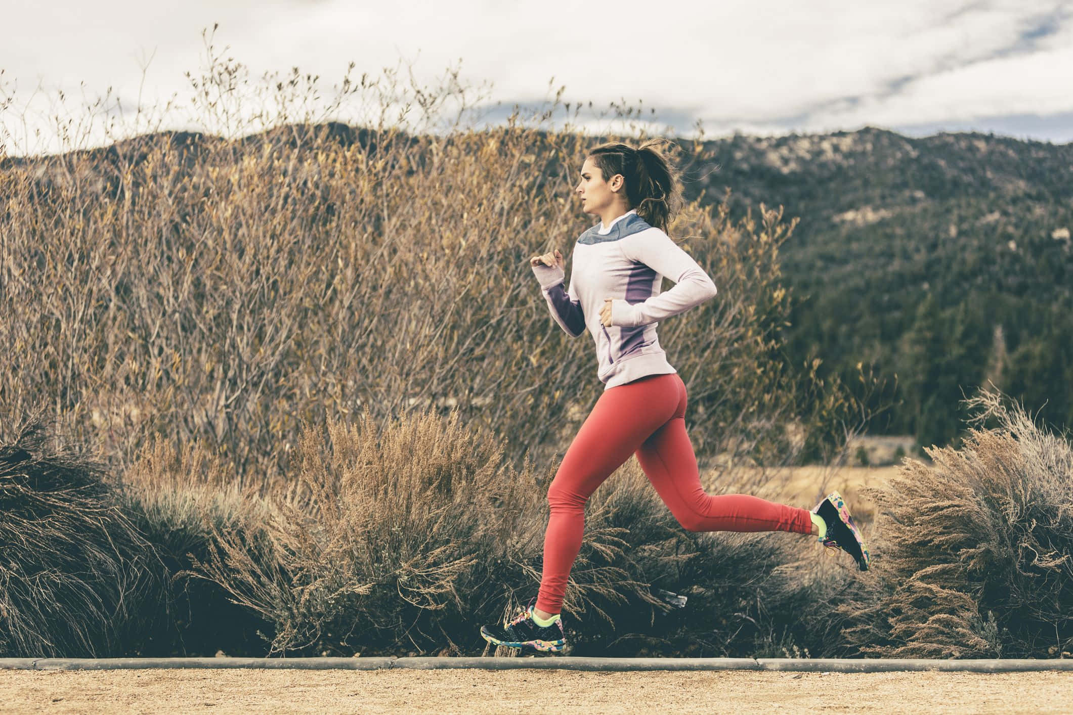 Running 桌布 壁紙 — 一位穿著紅色緊身褲的女性沿著一條泥路穿過乾草，背景有山。