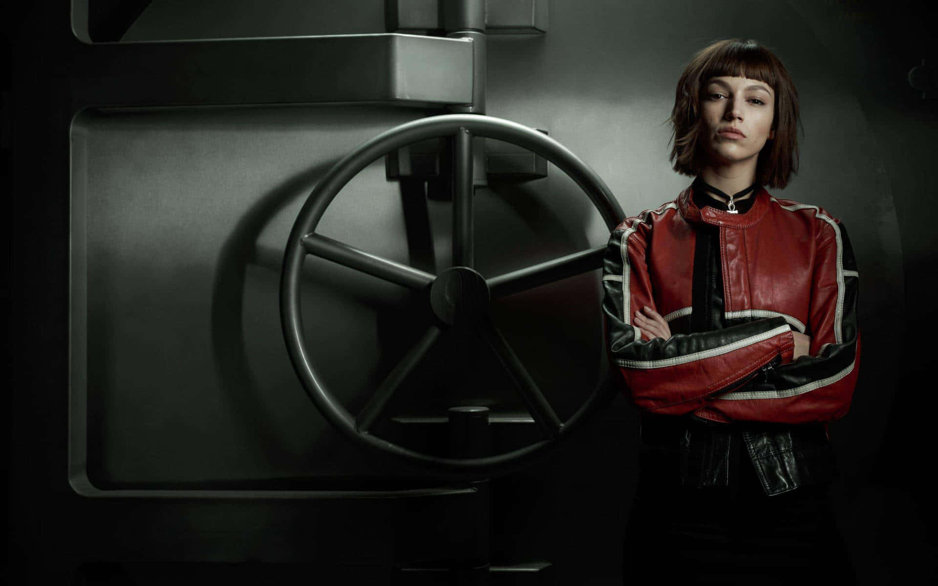 Money Heist 桌布 壁紙 — 一位穿著紅黑皮褸的女性自信地交叉雙臂，站在一個大型工業保險庫門旁。