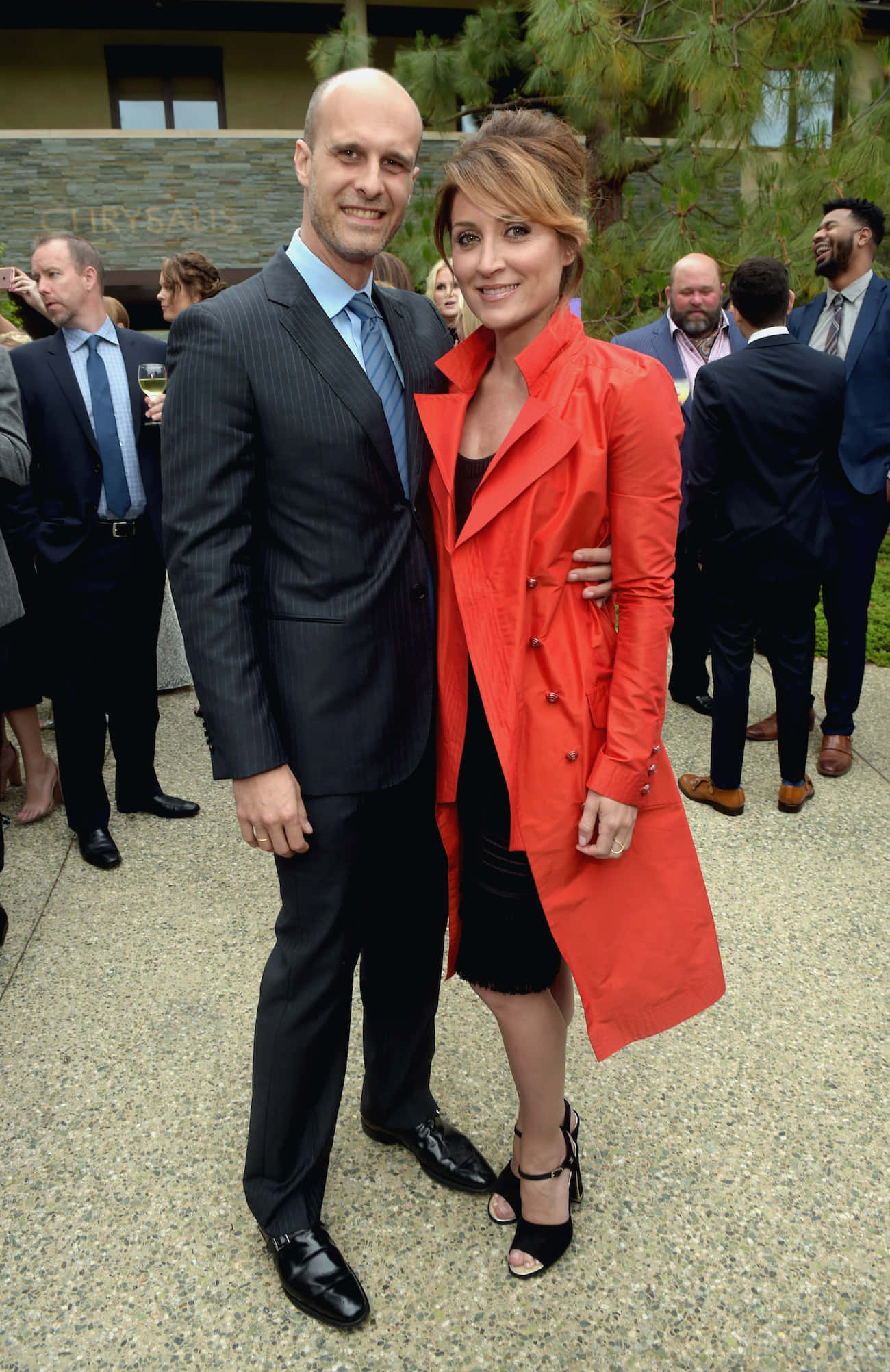 Sasha Alexander 桌布 壁紙 — 一位穿著細條紋西裝的男士和一位穿著鮮紅色外套的女士在戶外社交聚會中一起擺姿勢。