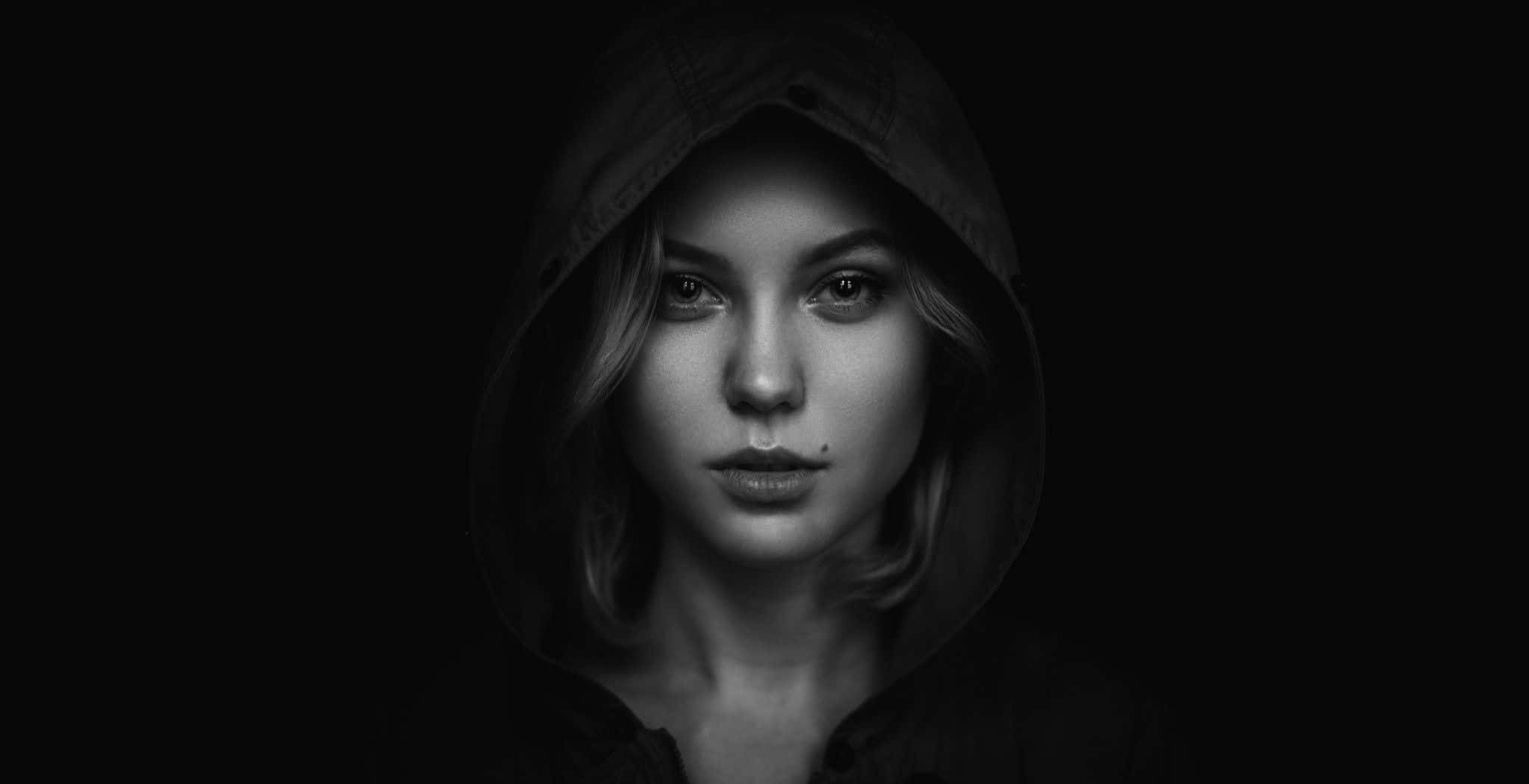 Black Is Beautiful 桌布 壁紙 — 一位穿著連帽外套的女性在黑色背景前，以高對比黑白肖像照中強烈凝視。