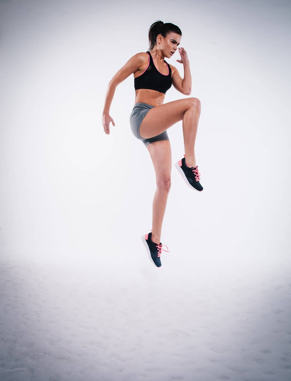 Athletic 桌布 壁紙 — 一位穿著運動服裝的健美女性在純白色工作室背景前動態跳躍。