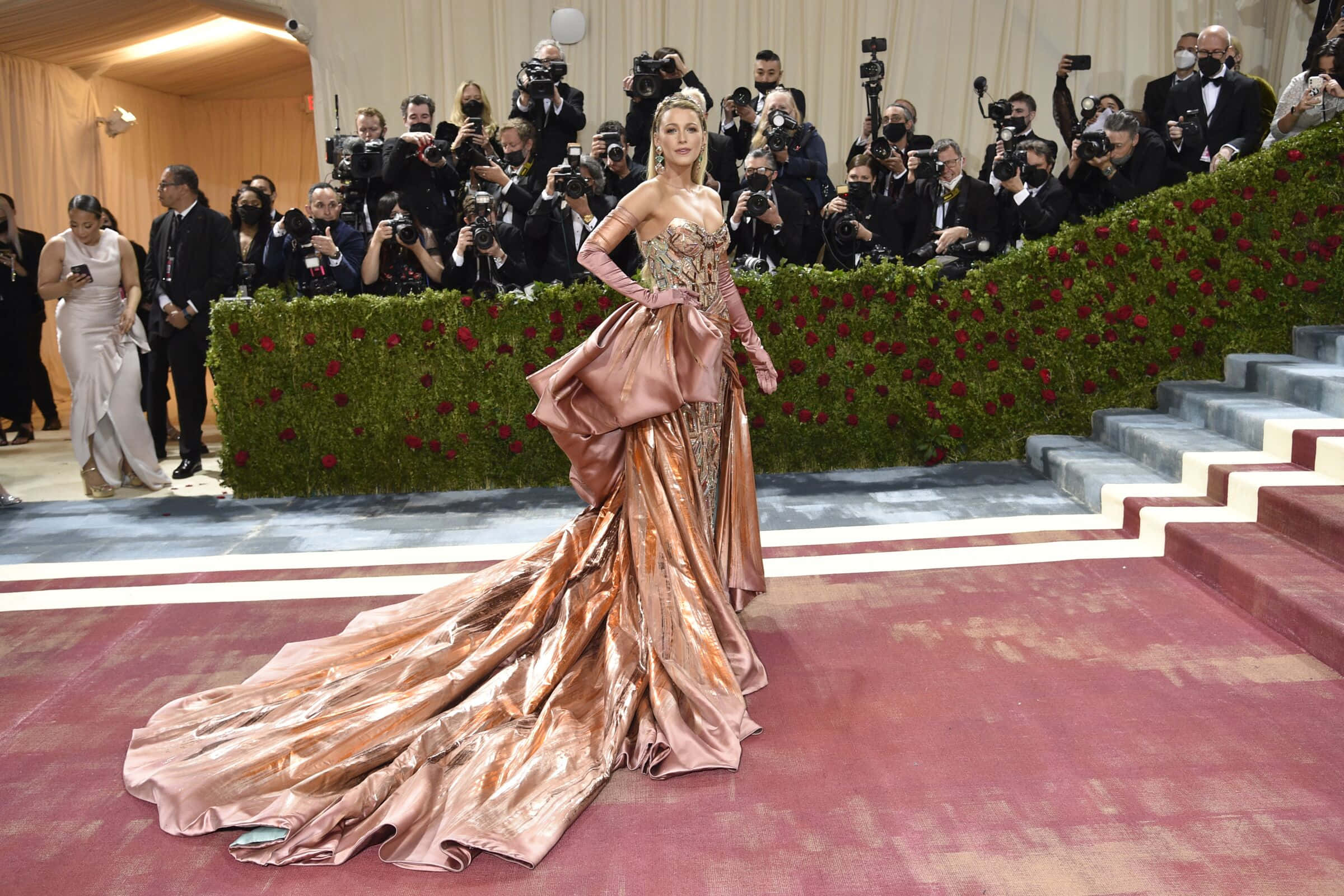 Met Gala 桌布 壁紙 — 一位穿著閃亮銅色禮服的迷人女性在紅地毯上擺姿勢，攝影師捕捉她在高調活動中的瞬間。