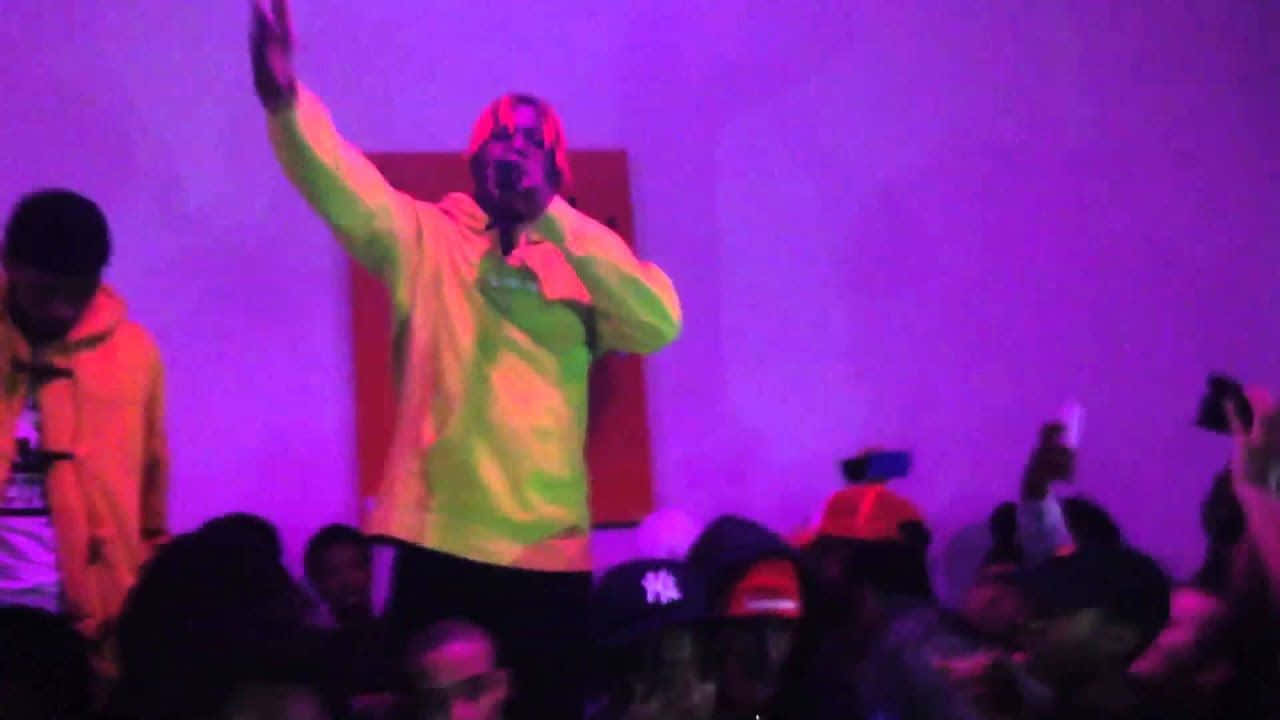 Lil Uzi Vert 桌布 壁紙 — 一位穿著霓虹外套的表演者在紫色舞台燈光下對著麥克風唱歌，下方有投入的觀眾。