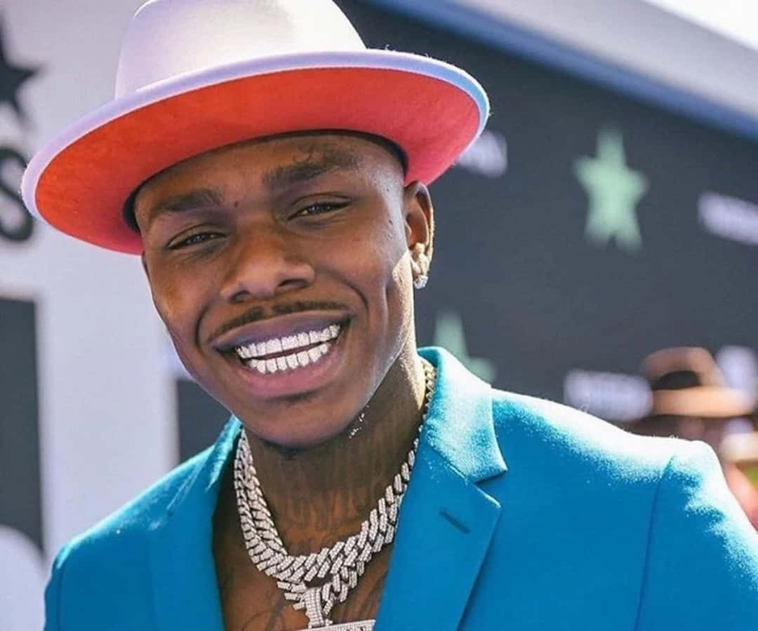 Dababy 桌布 壁紙 — 一位笑容滿面的男士身穿亮藍色西裝和彩色帽子，對著鏡頭露出閃亮的白牙。