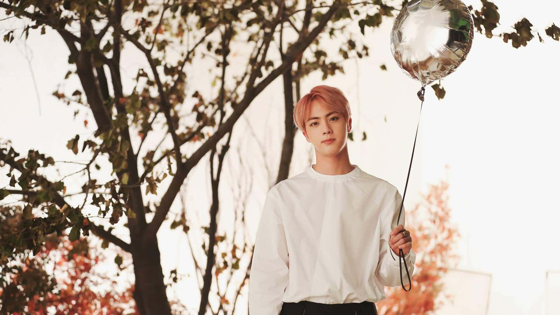 Jin 桌布 壁紙 — 一位粉紅色頭髮的年輕男子在柔和的金色光線穿過秋樹時，拿著一個銀色氣球。