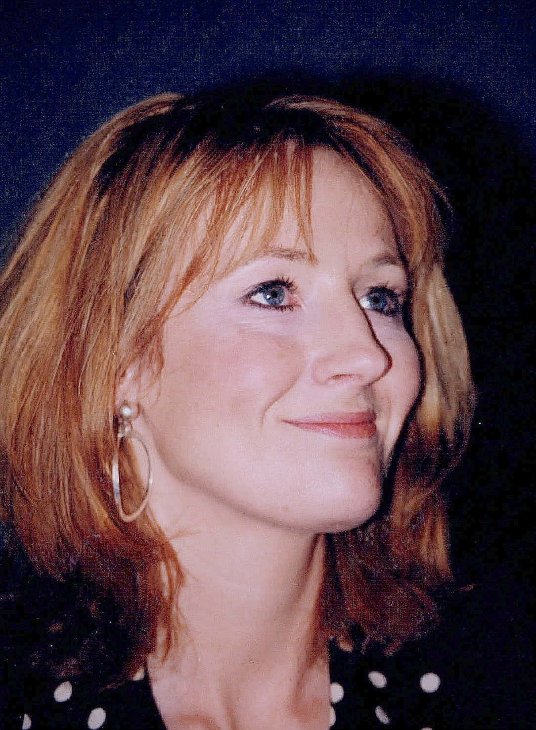 J K Rowling 桌布 壁紙 — 一位紅棕色頭髮、藍色眼睛的女性在深色背景下溫柔微笑的特寫肖像。