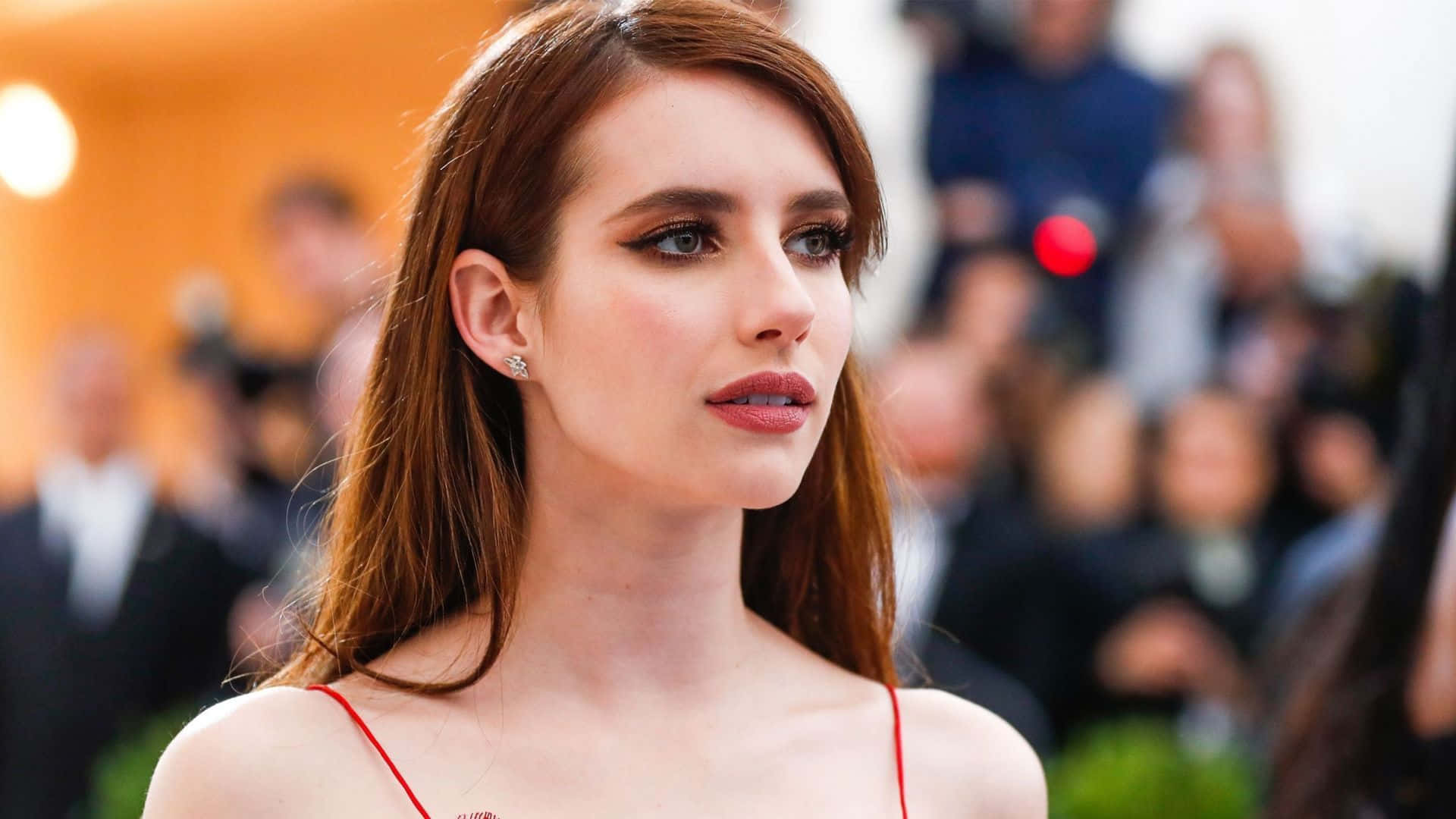 Met Gala 桌布 壁紙 — 一位紅髮、妝容大膽的迷人女士，在溫暖燈光下若有所思地凝視著擁擠的活動現場。