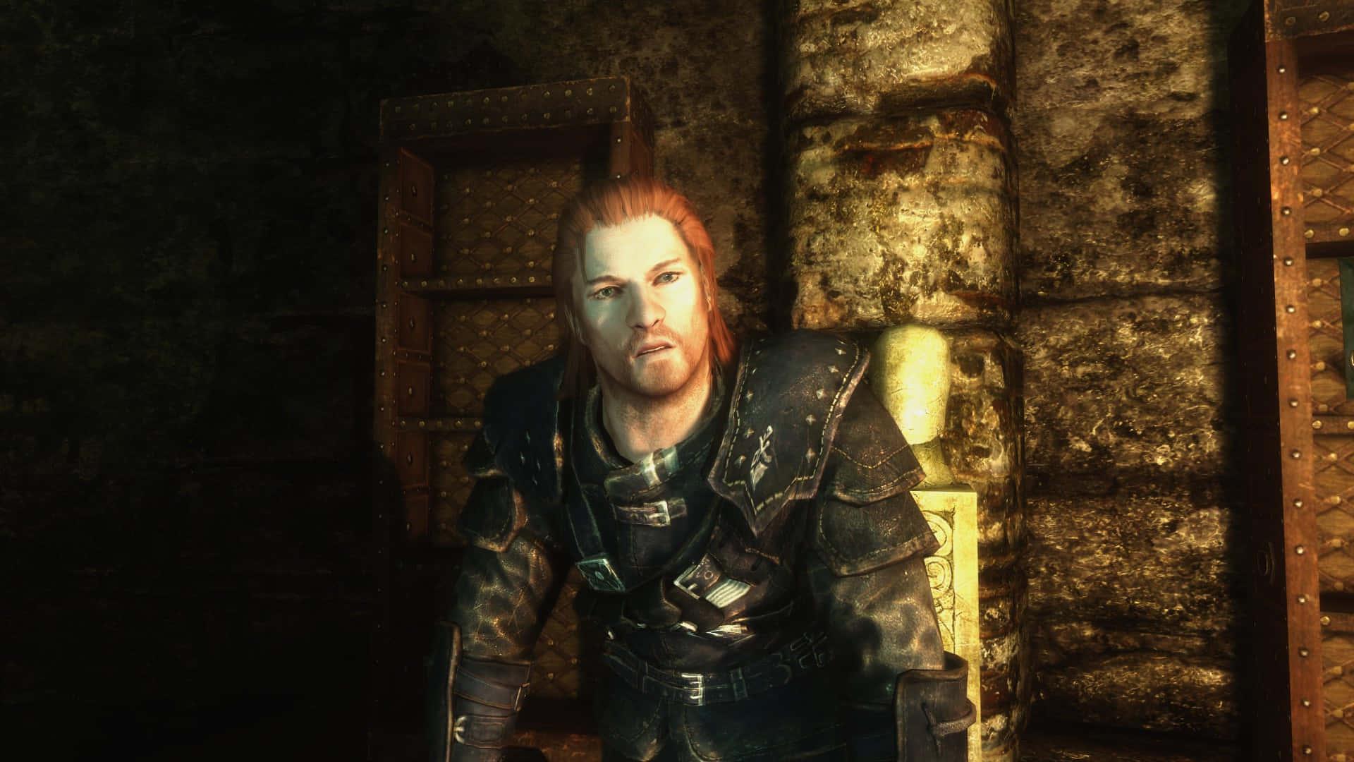 Skyrim Brynjolf 桌布 壁紙 — 一位紅髮戰士身穿暗色盔甲，在昏暗的地牢中倚靠著石牆，周圍有溫暖的環境光線。